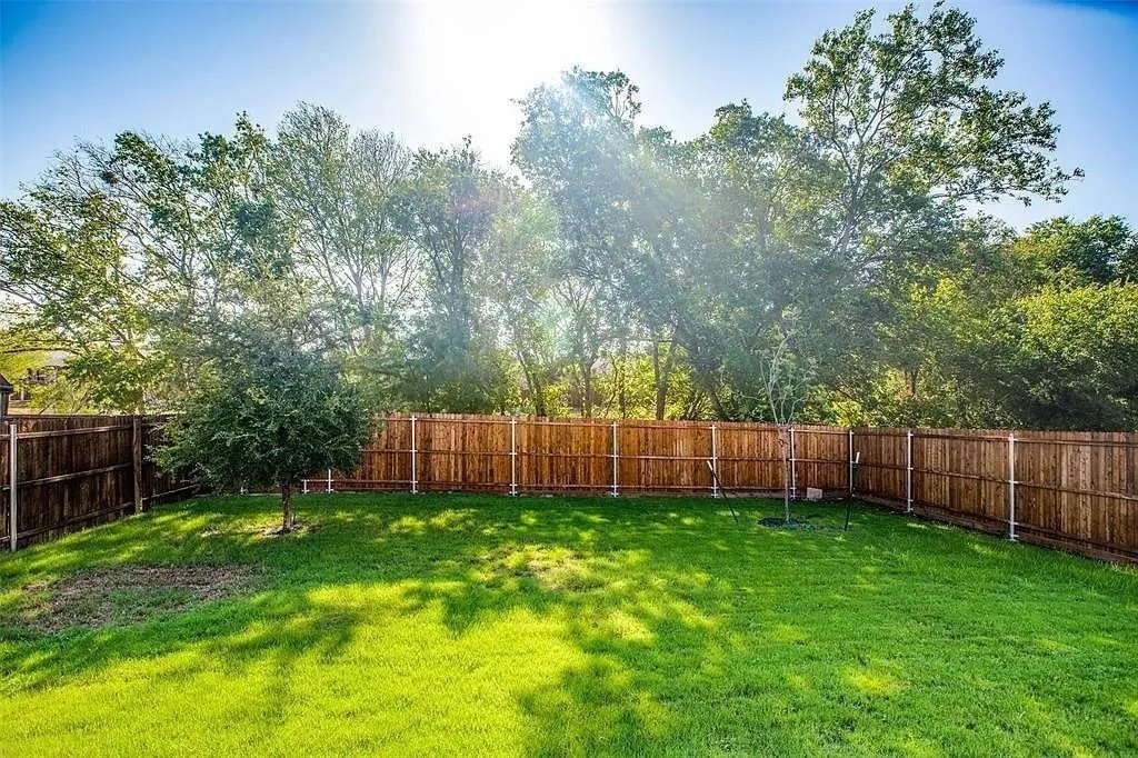 Expansive backyard featuring a manicured lawn, mature trees, and a full privacy fence