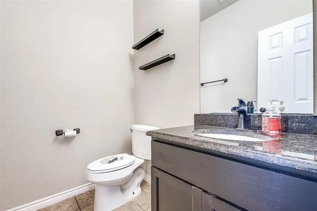 Floating shelves, dark wood-finish vanity, integrated sink, stone countertop, and tile flooring