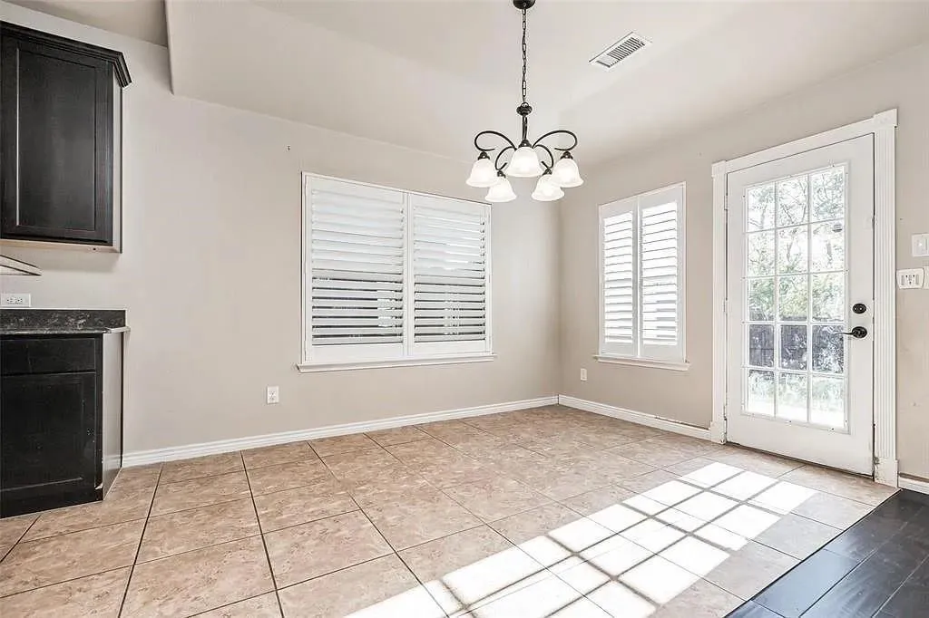 Recessed ceiling, tile flooring, two windows with plantation shutters, glass-paneled door, and a multi-arm chandelier