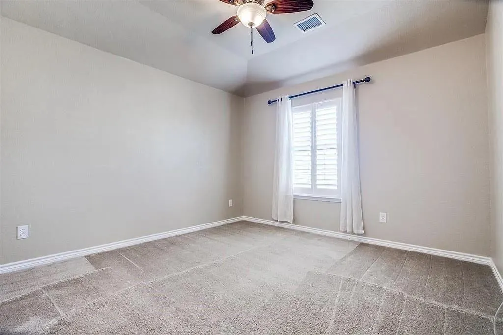 Tray ceiling with a ceiling fan, plantation shutters, and light gray walls