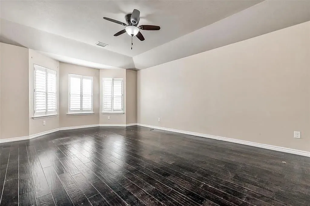 Vaulted ceiling with a ceiling fan, dark wood-finish flooring, and bay windows with plantation shutters