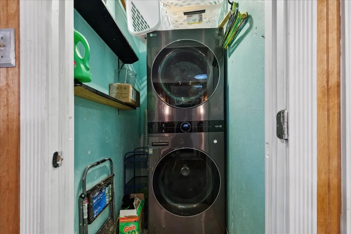 Stacked laundry appliances, built-in shelving, and a wall-mounted shelf provide storage solutions within the utility area