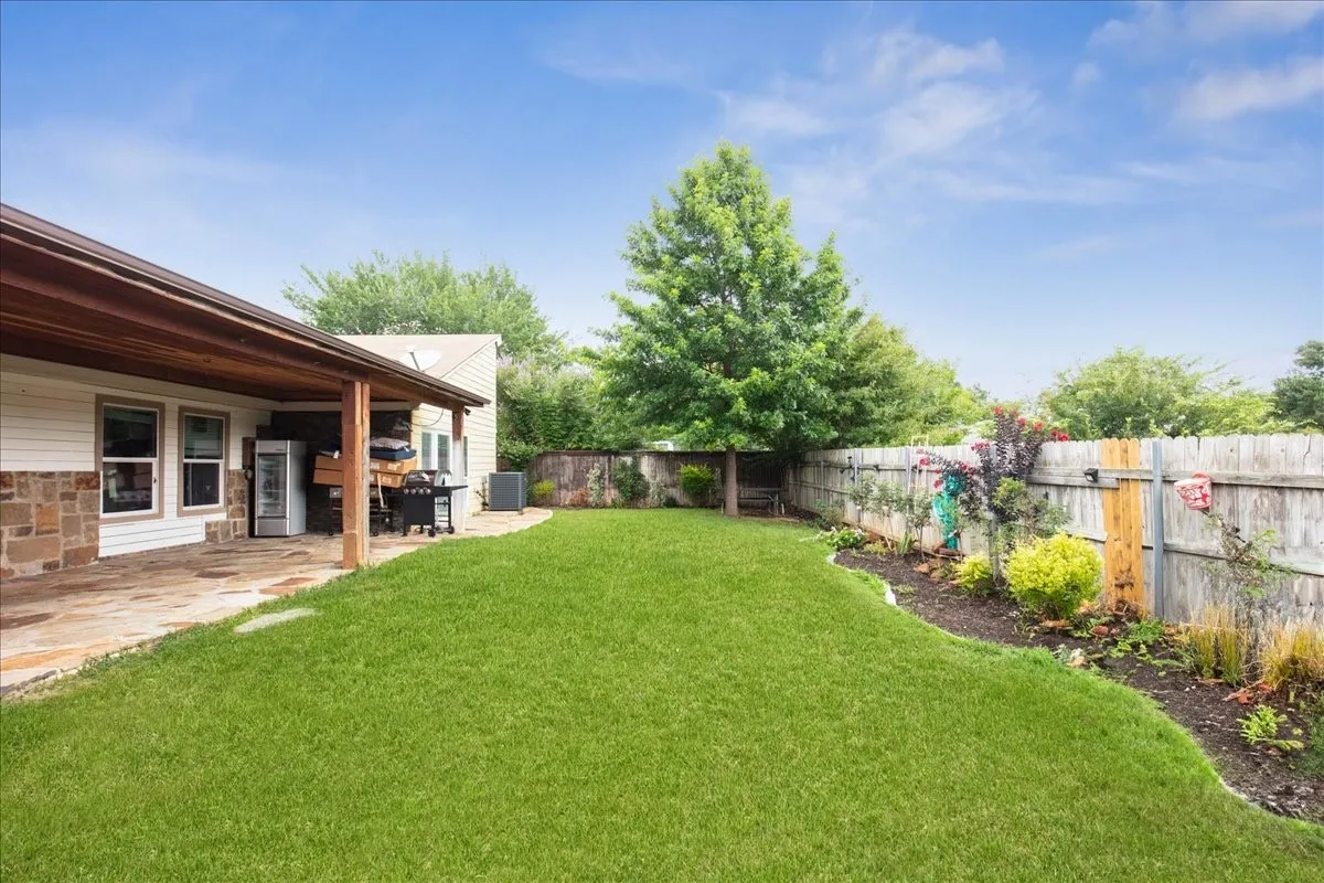 Expansive grass lawn with a stone patio and wood-covered outdoor living area