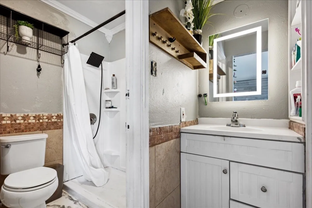 Bathroom featuring a white vanity with integrated sink, an illuminated mirror, and a shower with a black fixture