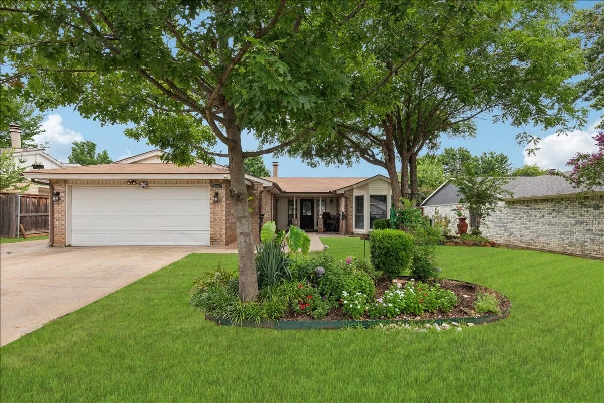Brick exterior with an attached garage, paved driveway, and mature landscaping