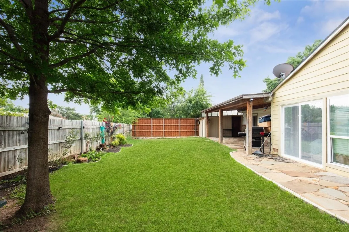 Expansive backyard with a manicured lawn, established tree, wood fencing, covered patio, and flagstone pathway