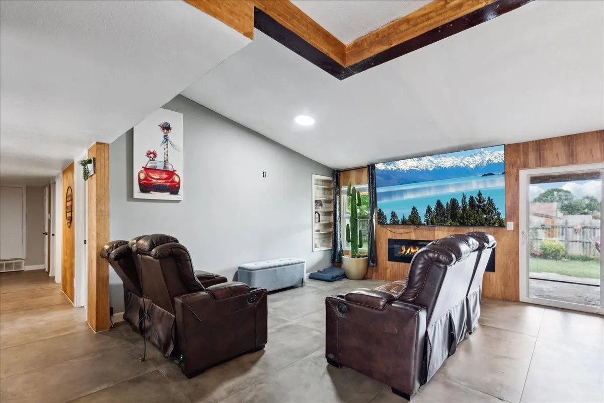 Vaulted ceiling with exposed wood beams, built-in electric fireplace, wood panel accent wall, and concrete-finish flooring