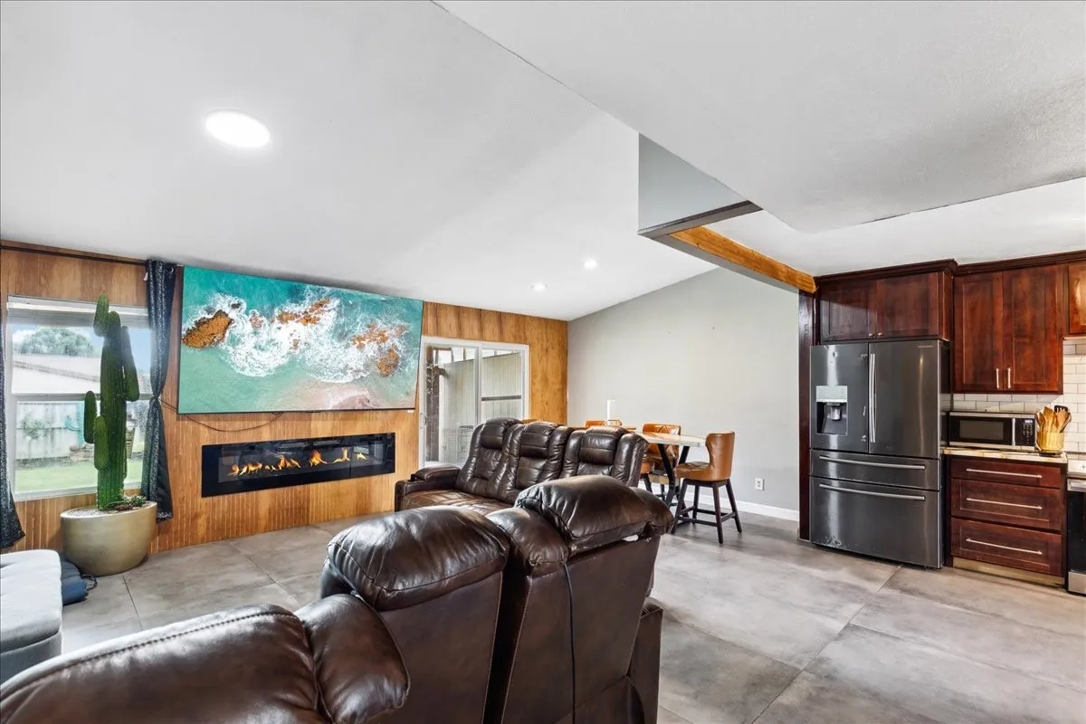 Vaulted ceiling with recessed lighting, linear electric fireplace, wood-finish wall paneling, tile flooring, and dark wood-finish cabinetry
