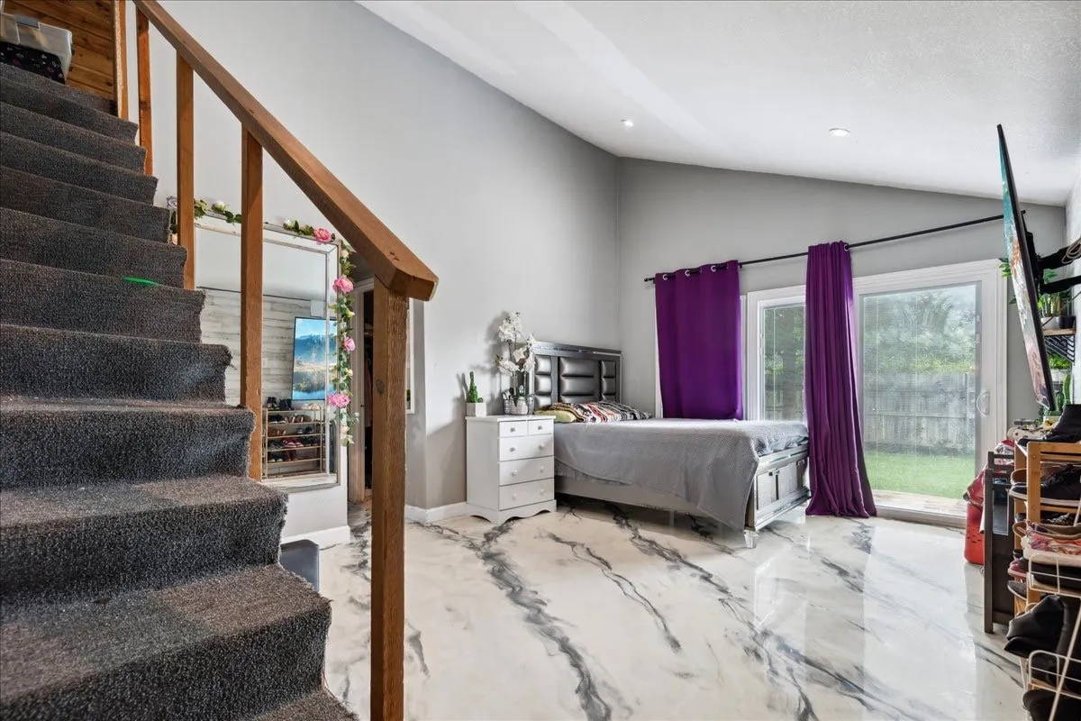 Vaulted ceiling with recessed lighting, wood-finish stair railing, gray carpeted stairs, white and gray marbled flooring, and sliding glass door access to exterior