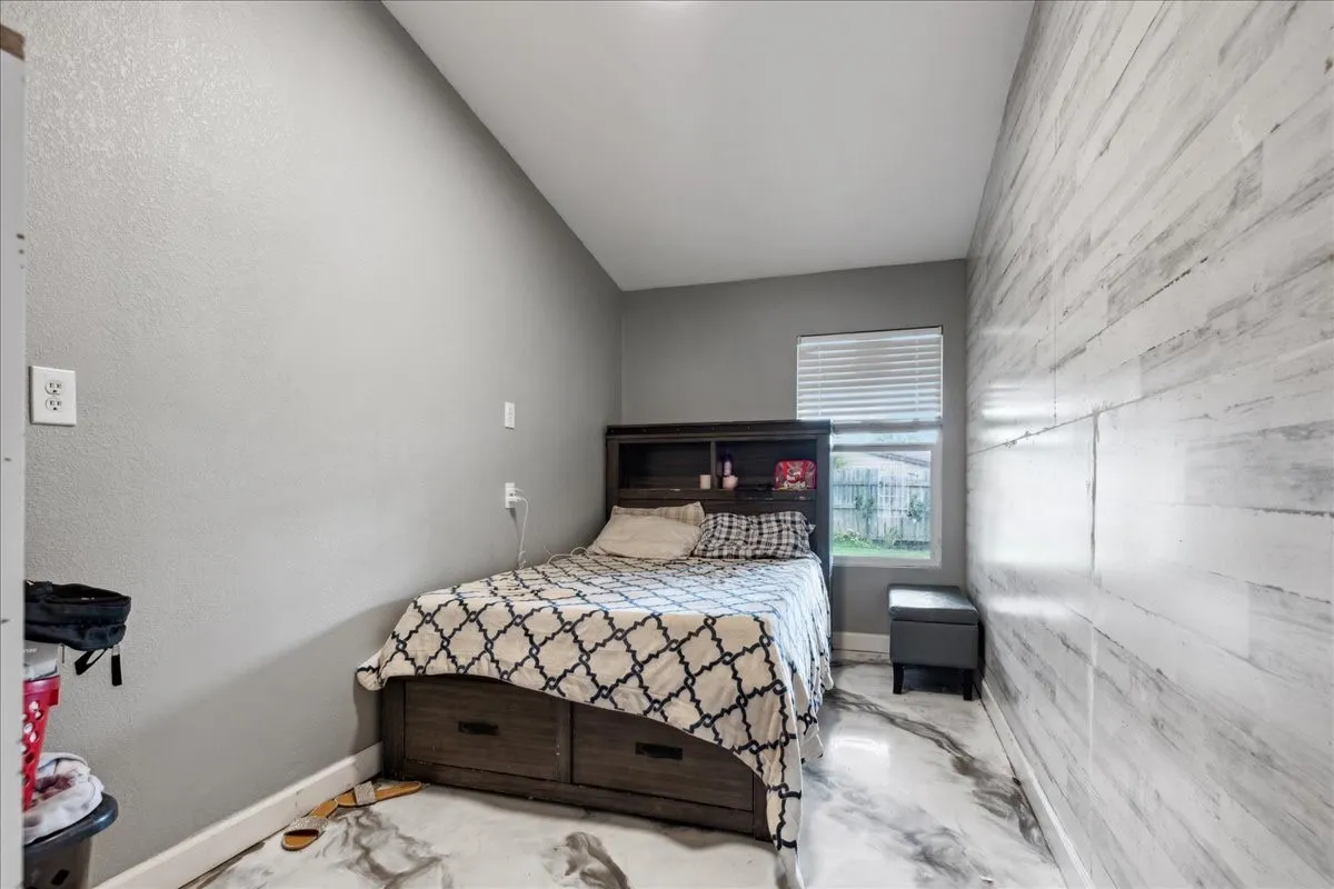 Angled ceiling, light gray painted walls, window with blinds, wood-finish accent wall, and marble-look flooring