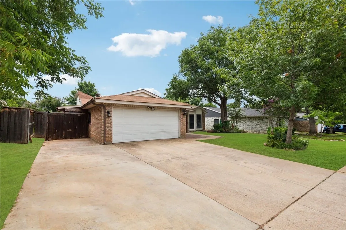 Brick exterior with an attached garage, concrete driveway, and mature landscaping
