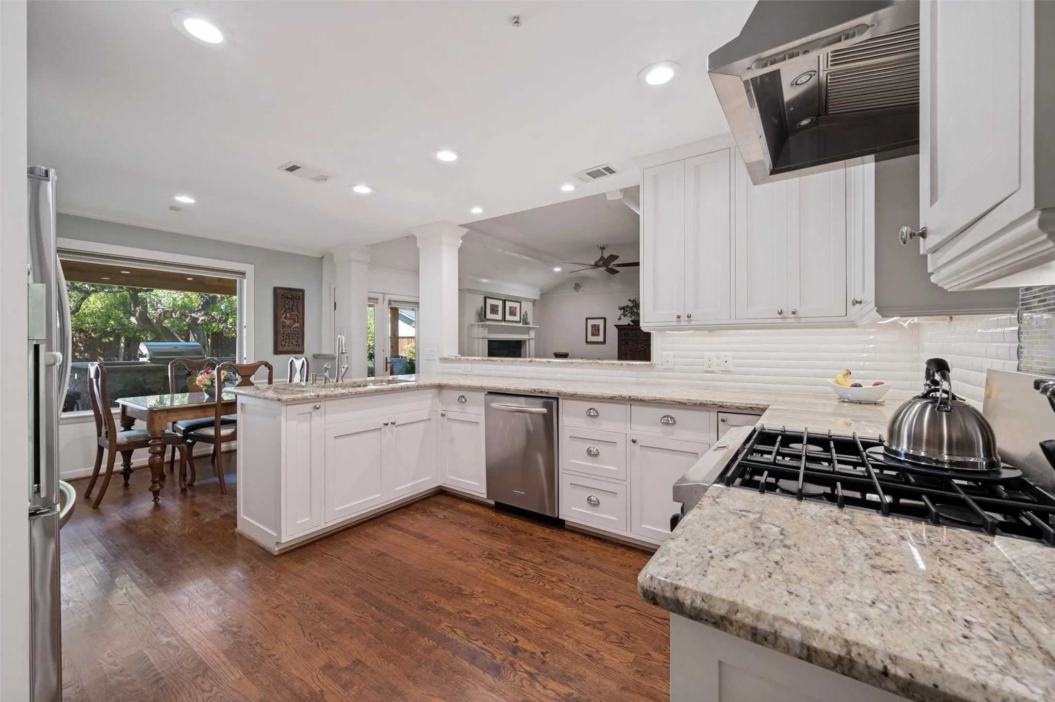 Wood-finish flooring, white cabinetry, integrated stainless steel appliances, granite countertops, and recessed lighting