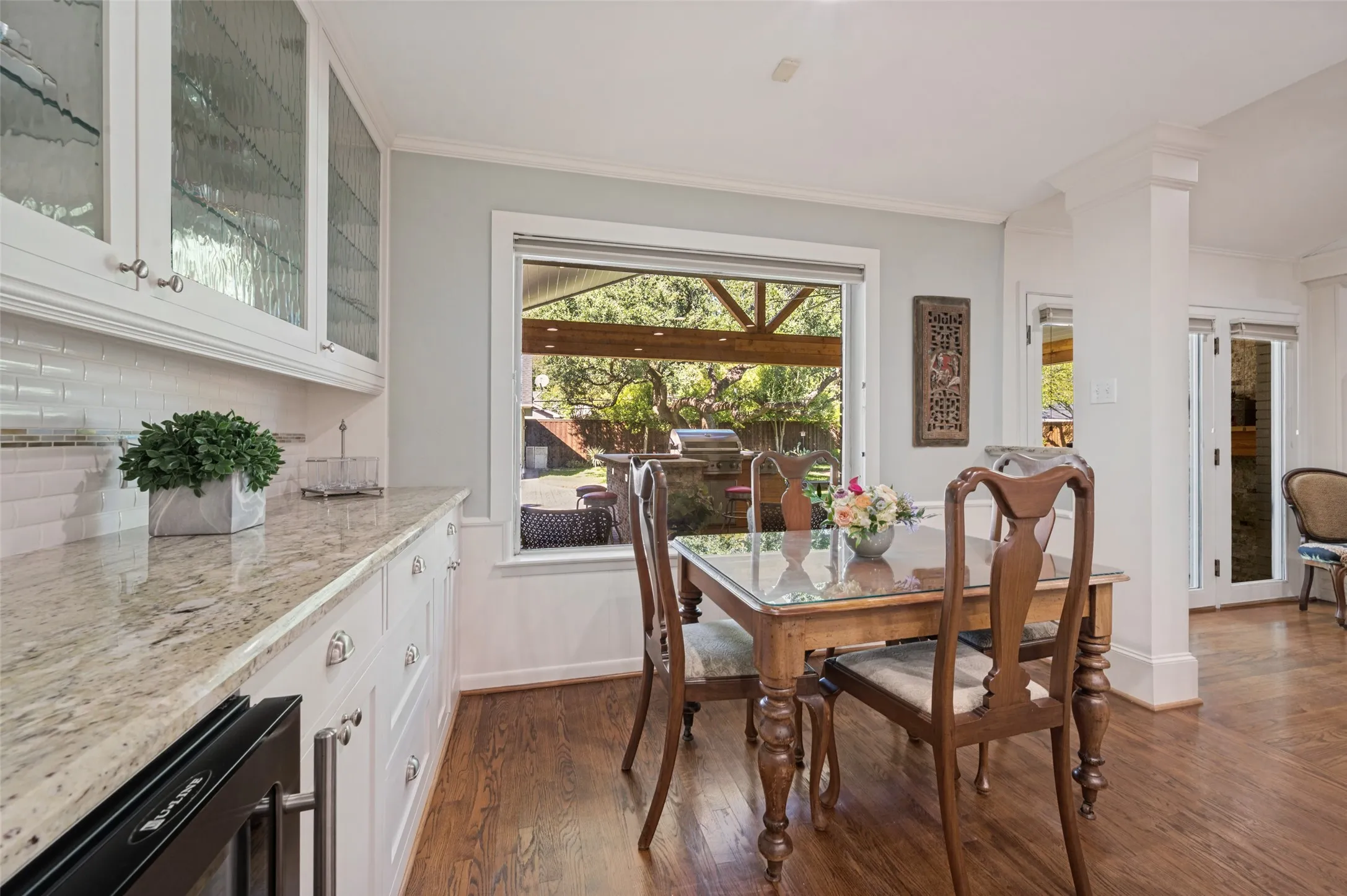 White cabinetry with glass-front uppers, granite countertops, subway tile backsplash, wood-finish flooring, and a large picture window