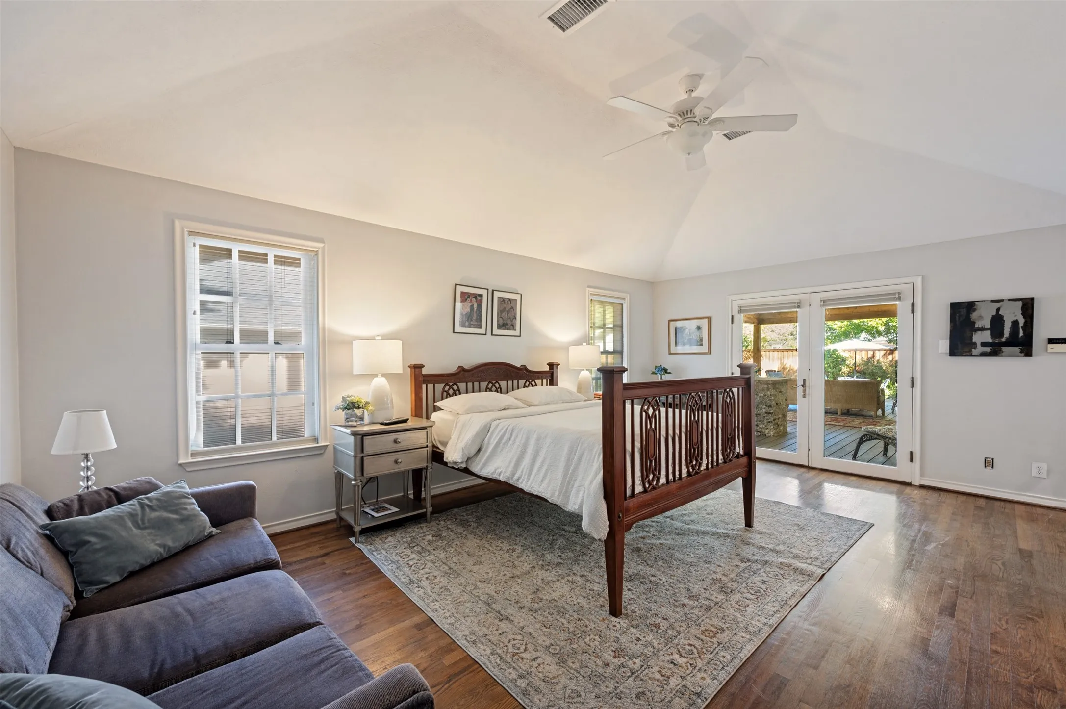 Vaulted ceiling with a ceiling fan, hardwood flooring, white double-pane windows, and patio access via glass French doors