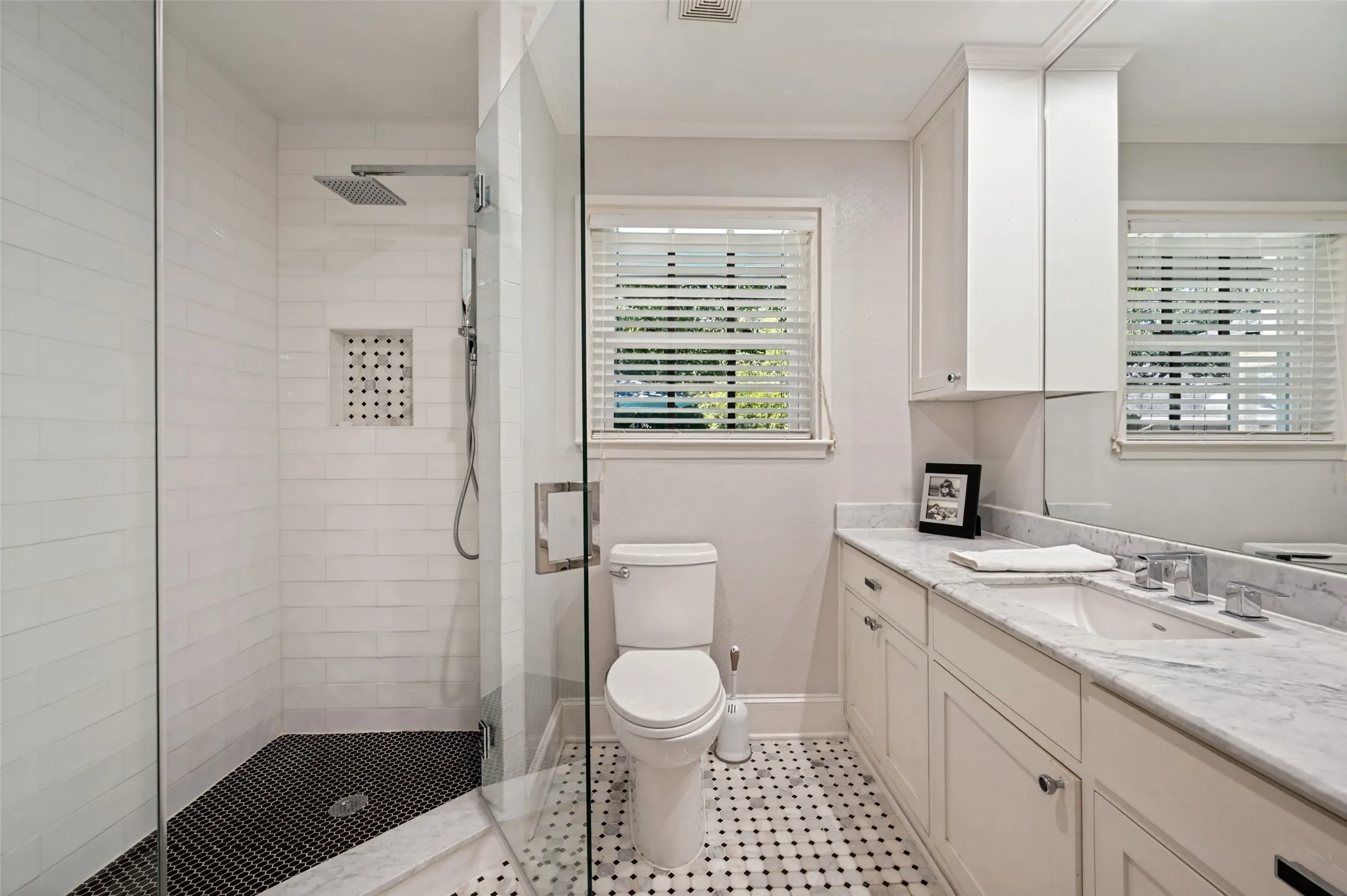 Shower with glass enclosure and rain-style showerhead, mosaic tile flooring, white subway tile shower walls, marble vanity with built-in cabinetry, and marble-finish countertop