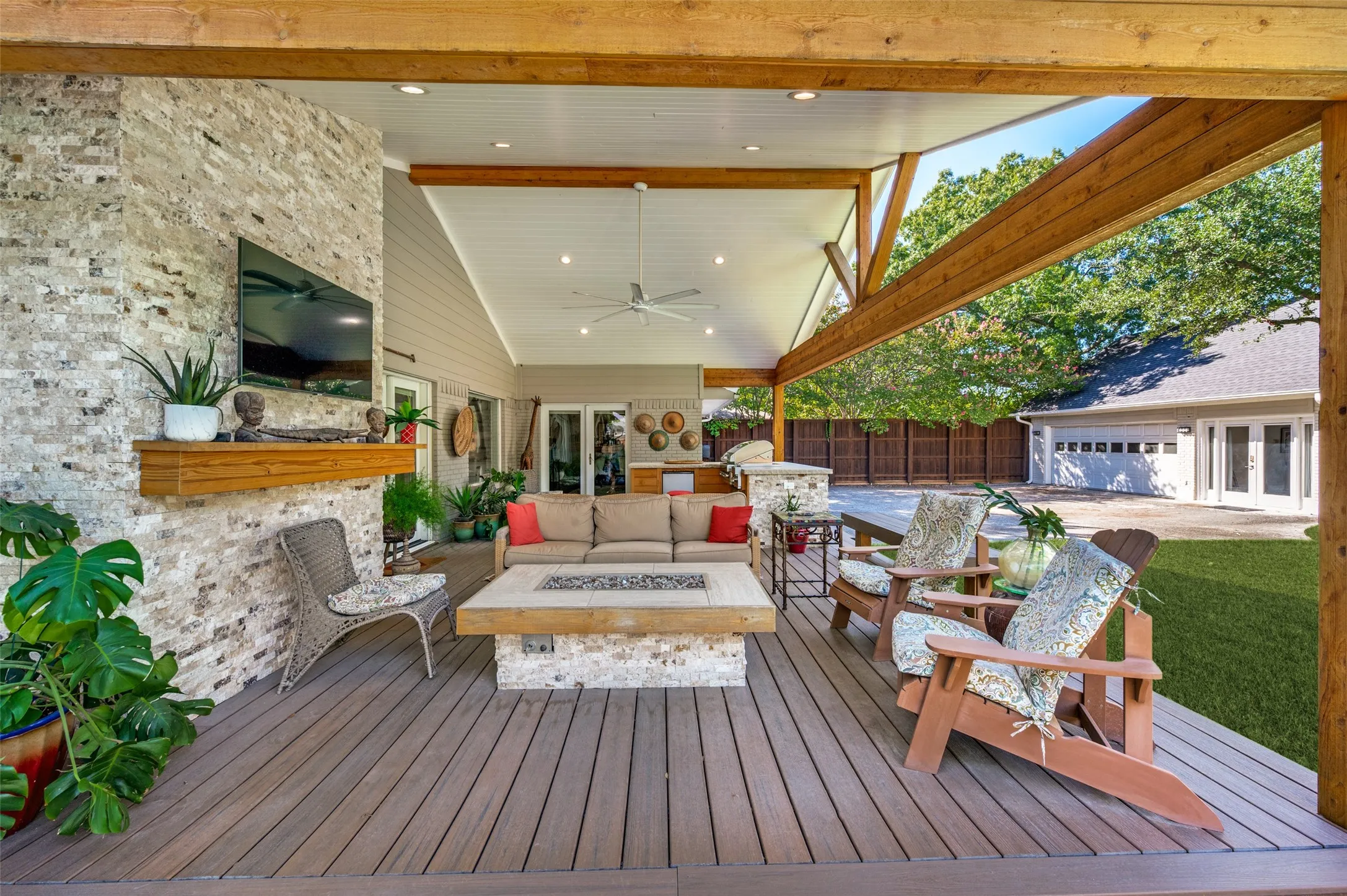 Covered outdoor living space featuring vaulted ceilings, exposed wood beams, a stone-clad fireplace, and an integrated outdoor kitchen