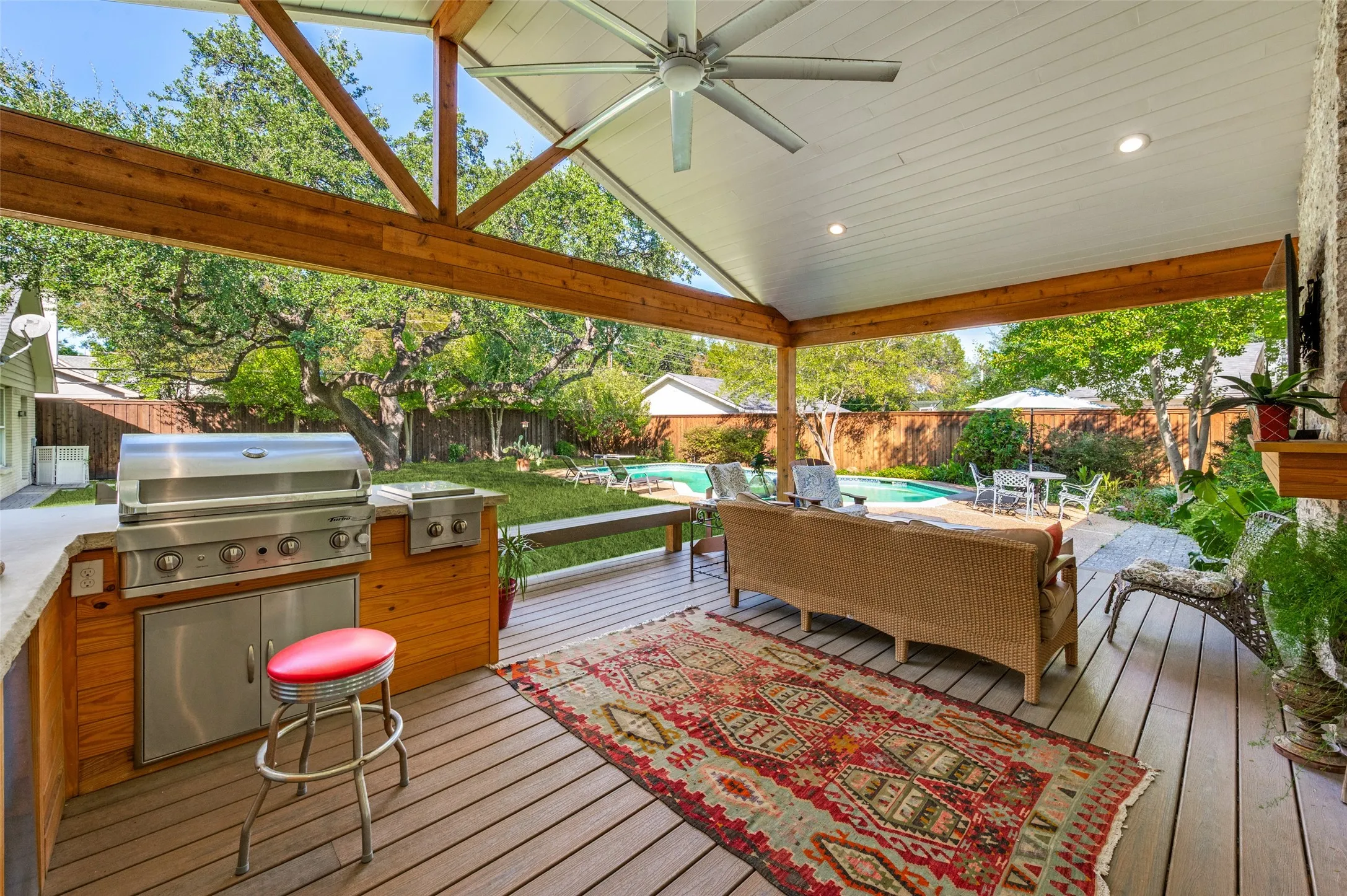 Expansive covered patio with exposed wood beams, composite decking, built-in outdoor kitchen, recessed lighting, and ceiling fan