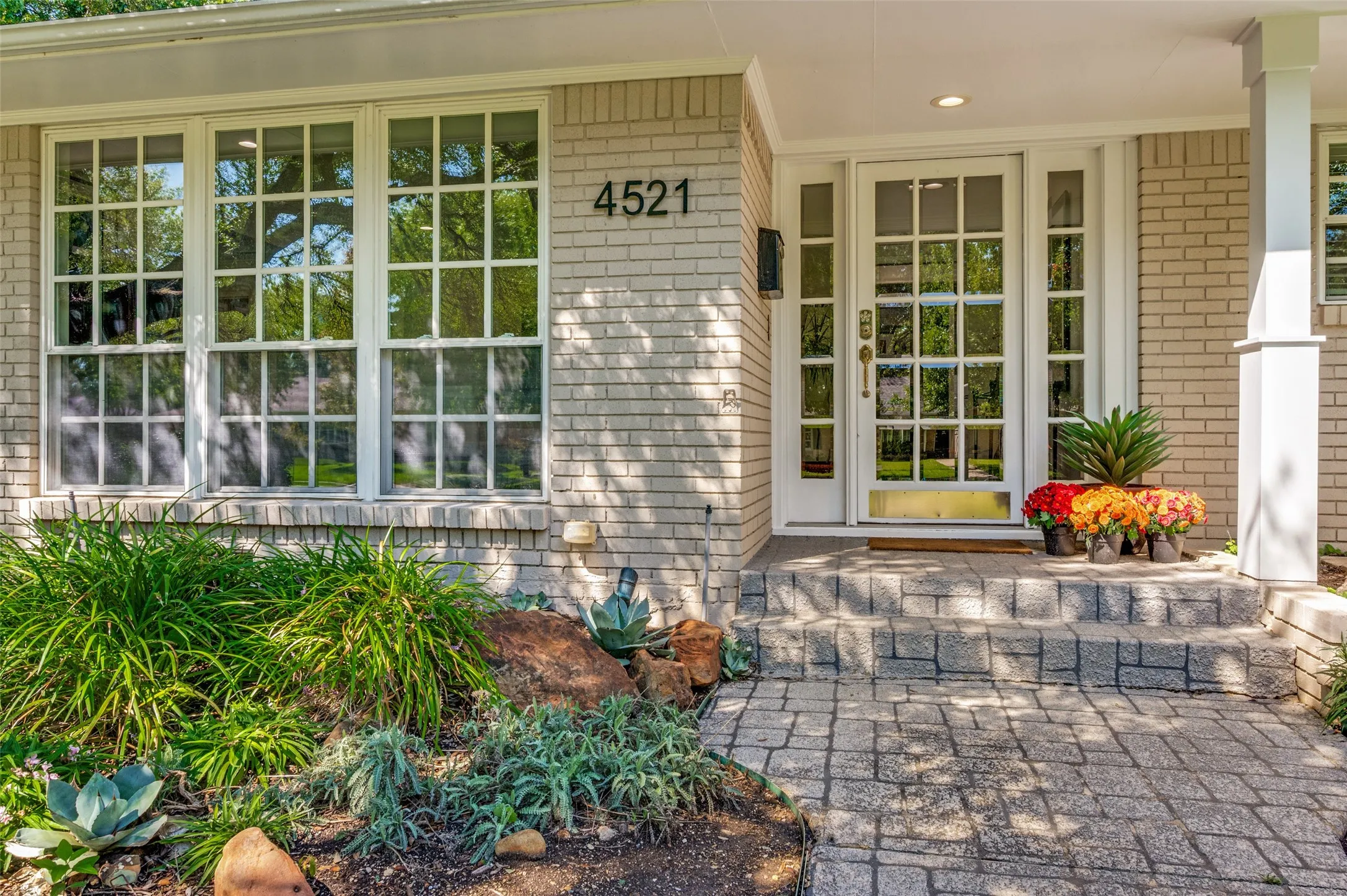 Light-colored brick exterior with multiple windows, a glass-paned front door, and a stone-tiled entryway