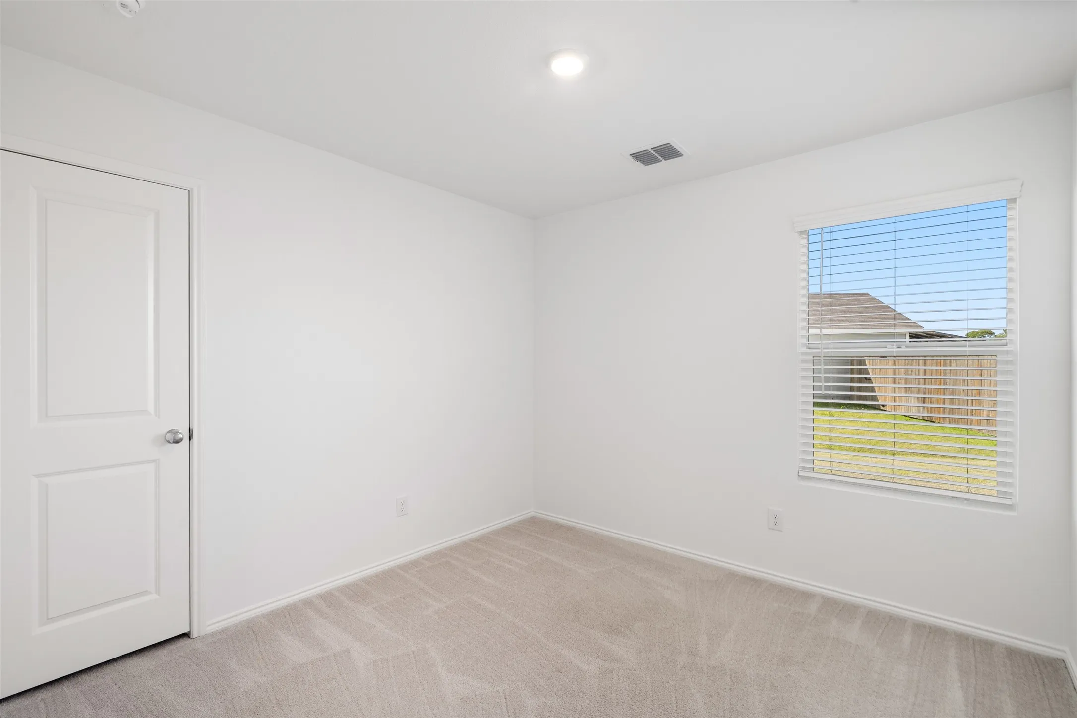 Neutral color palette with light gray carpeting, recessed ceiling light, and window with blinds