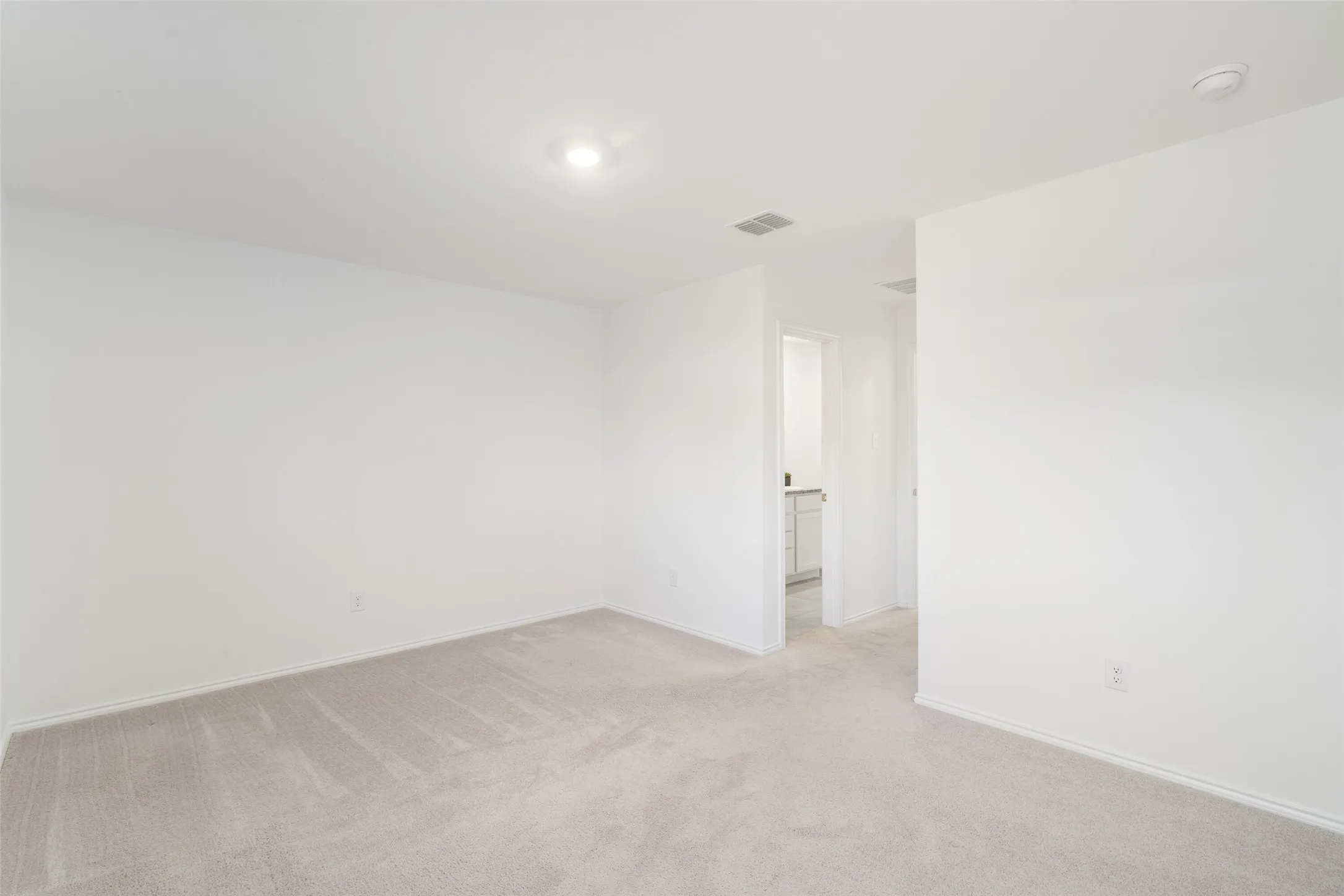 Spacious room featuring neutral carpeting and white wall finishes, with recessed lighting and a doorway leading to an additional space
