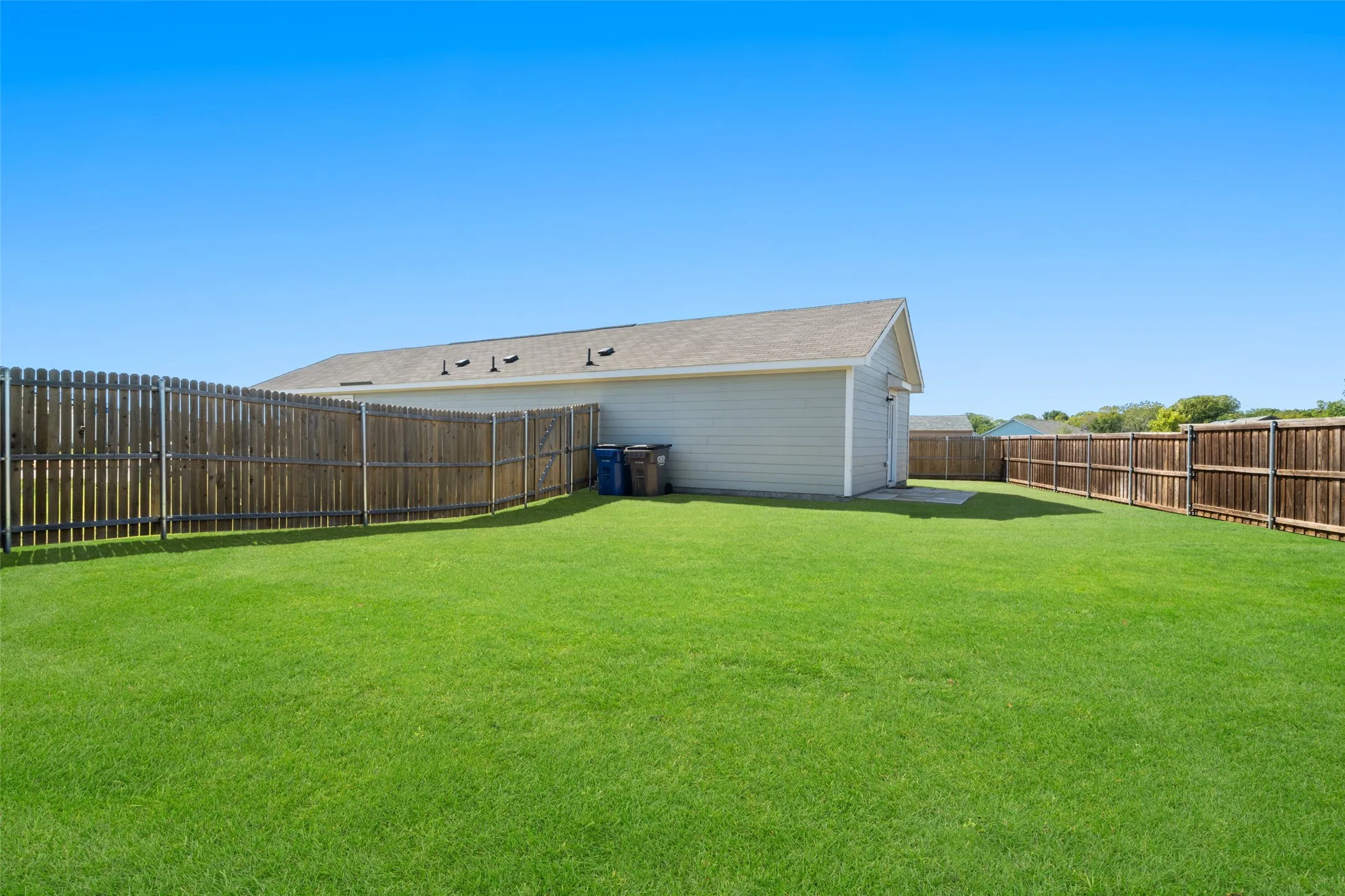 Expansive green lawn, wood privacy fencing, light-colored siding, and a gabled roofline