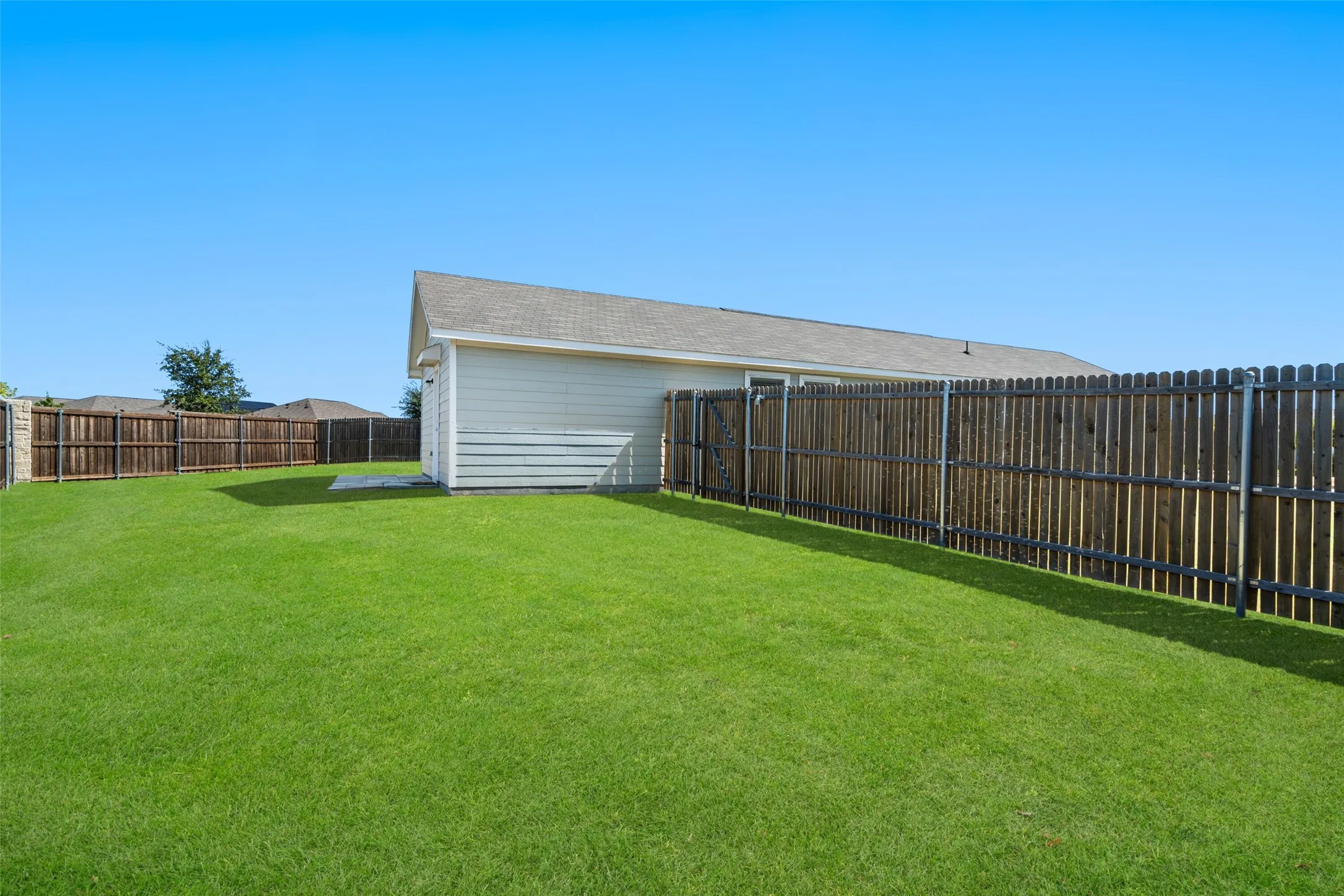 Expansive lawn area, full wood privacy fencing, concrete patio, and a detached structure with siding and a shingled roof