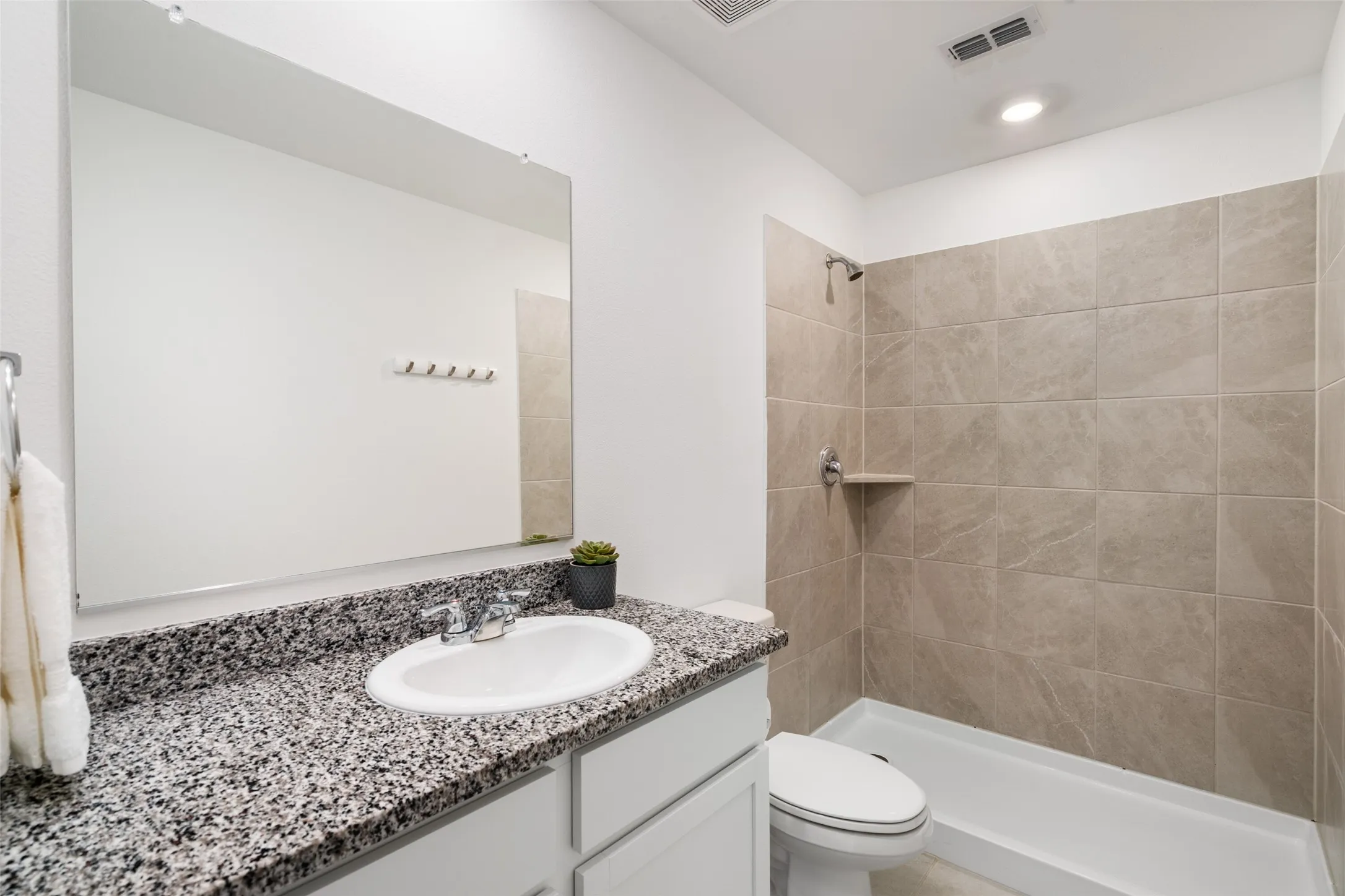 Granite-look countertop, undermount sink, large mirror, and tiled shower surround with built-in shelf