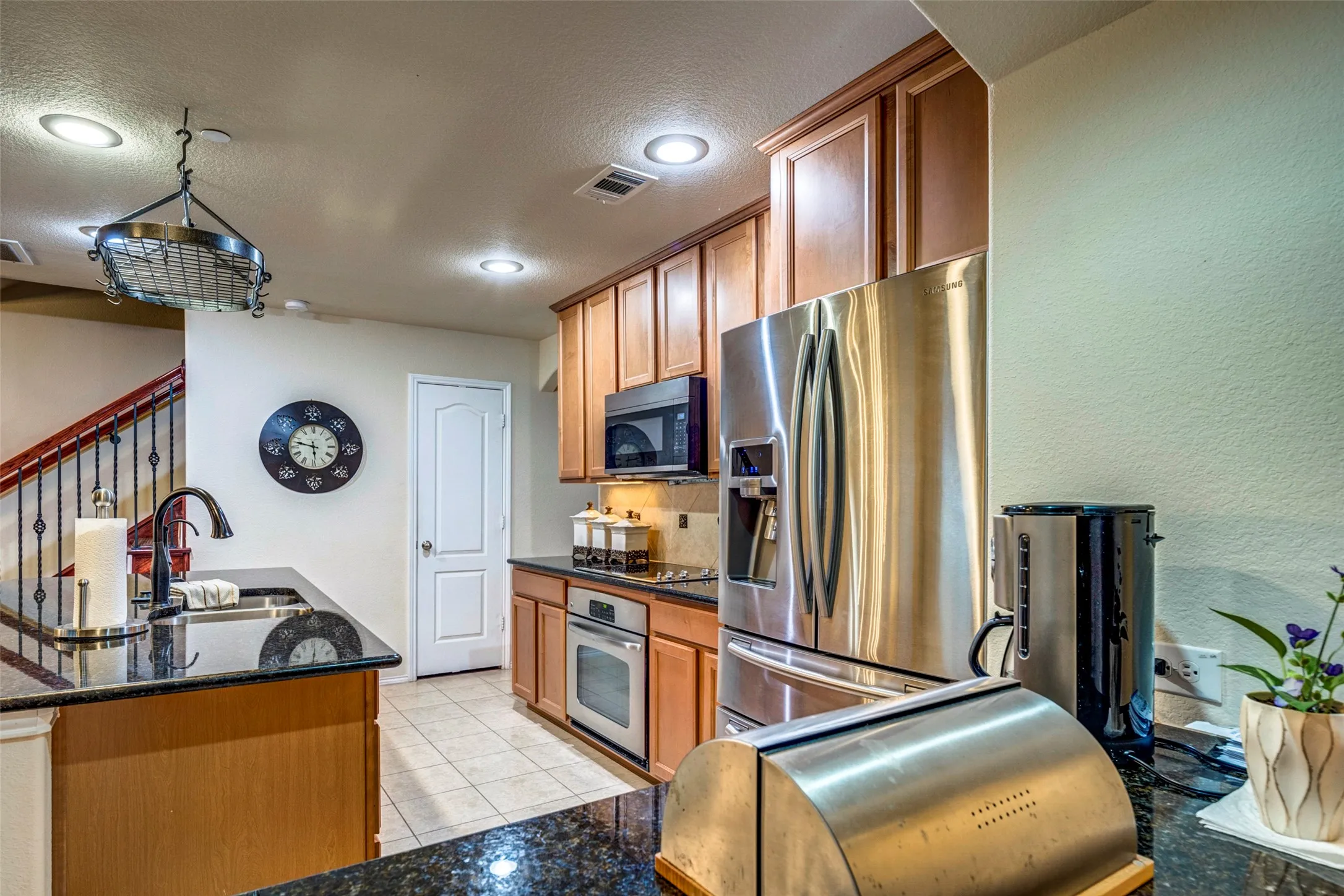 Kitchen featuring black granite countertops, stainless steel appliances, wood cabinetry, recessed lighting, and tile flooring