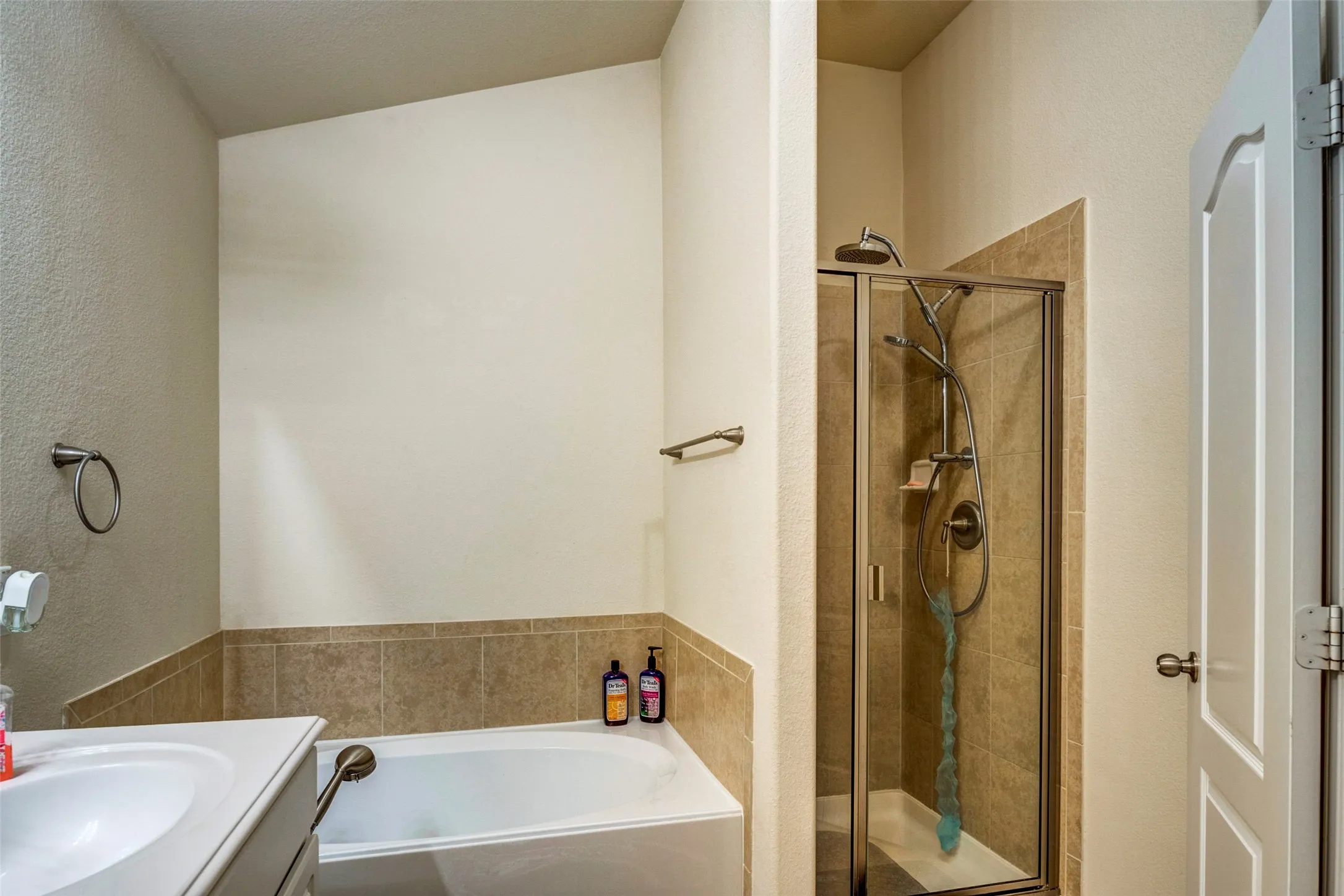 Master bathroom featuring dual vanity with white ceramic sink, tile-accented wall surround, soaking tub, and separate walk-in shower with glass enclosure and bronze fixtures