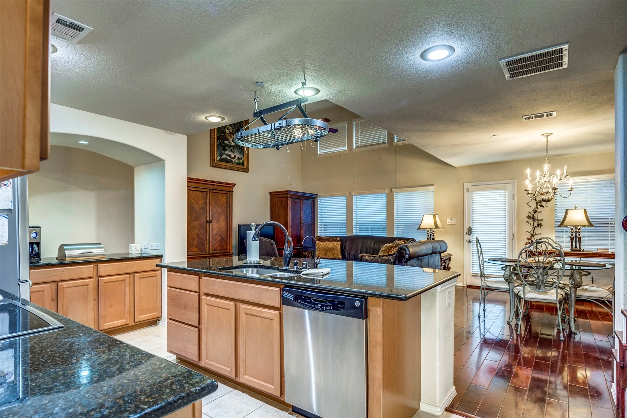 Kitchen featuring granite countertops, wood cabinetry, stainless steel dishwasher, and a center island with sink