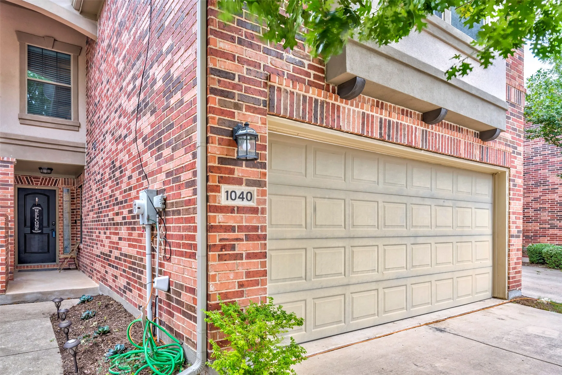 Charming brick home at 1040 featuring a spacious two-car garage with paneled overhead door, manicured front landscaping with mature greenery, and classic red brick exterior with architectural detail