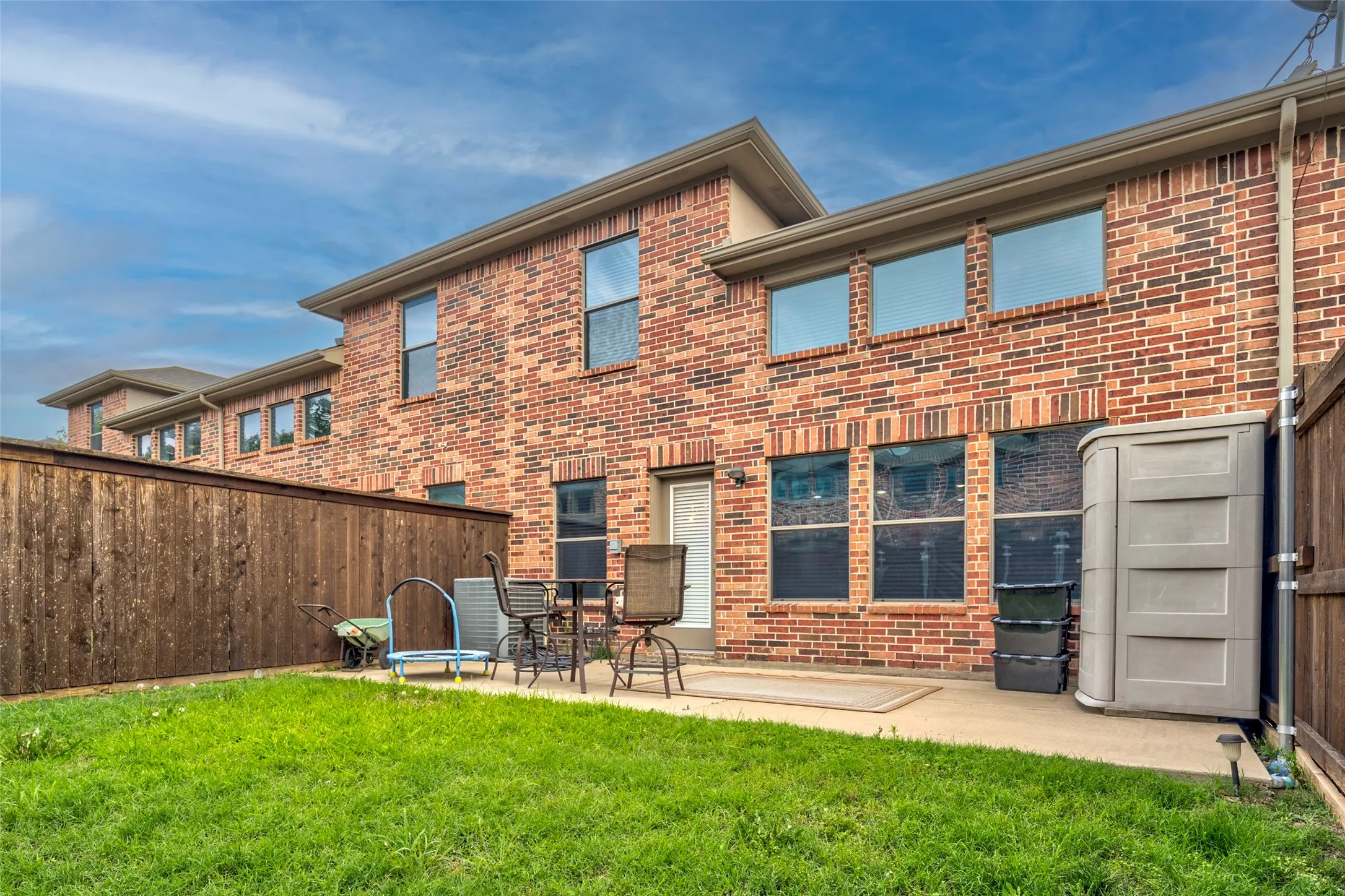 Brick exterior with expansive rear patio featuring a concrete surface and manicured lawn