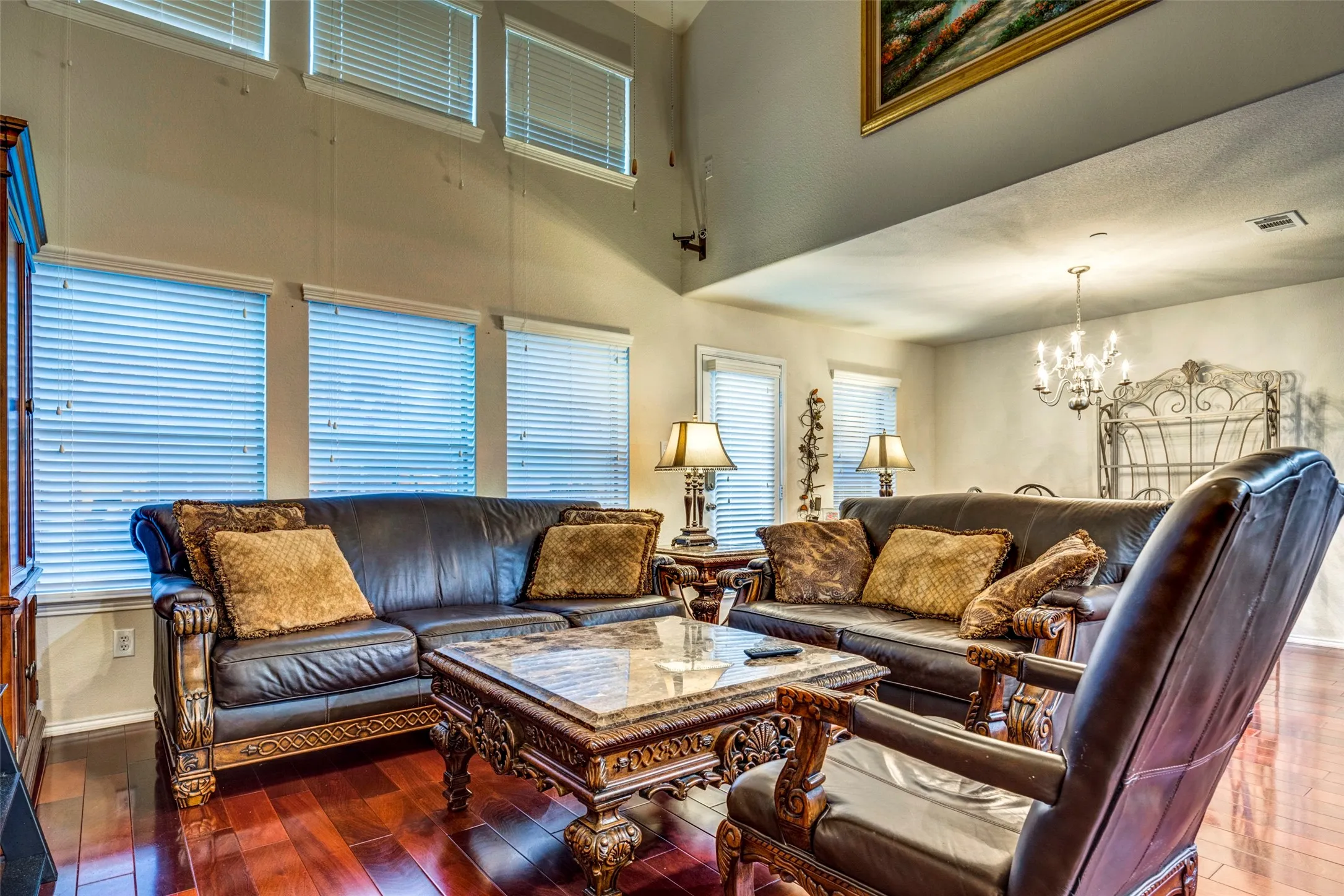 High vaulted ceiling, multiple windows with blinds, wood-finish flooring, and a chandelier lighting fixture