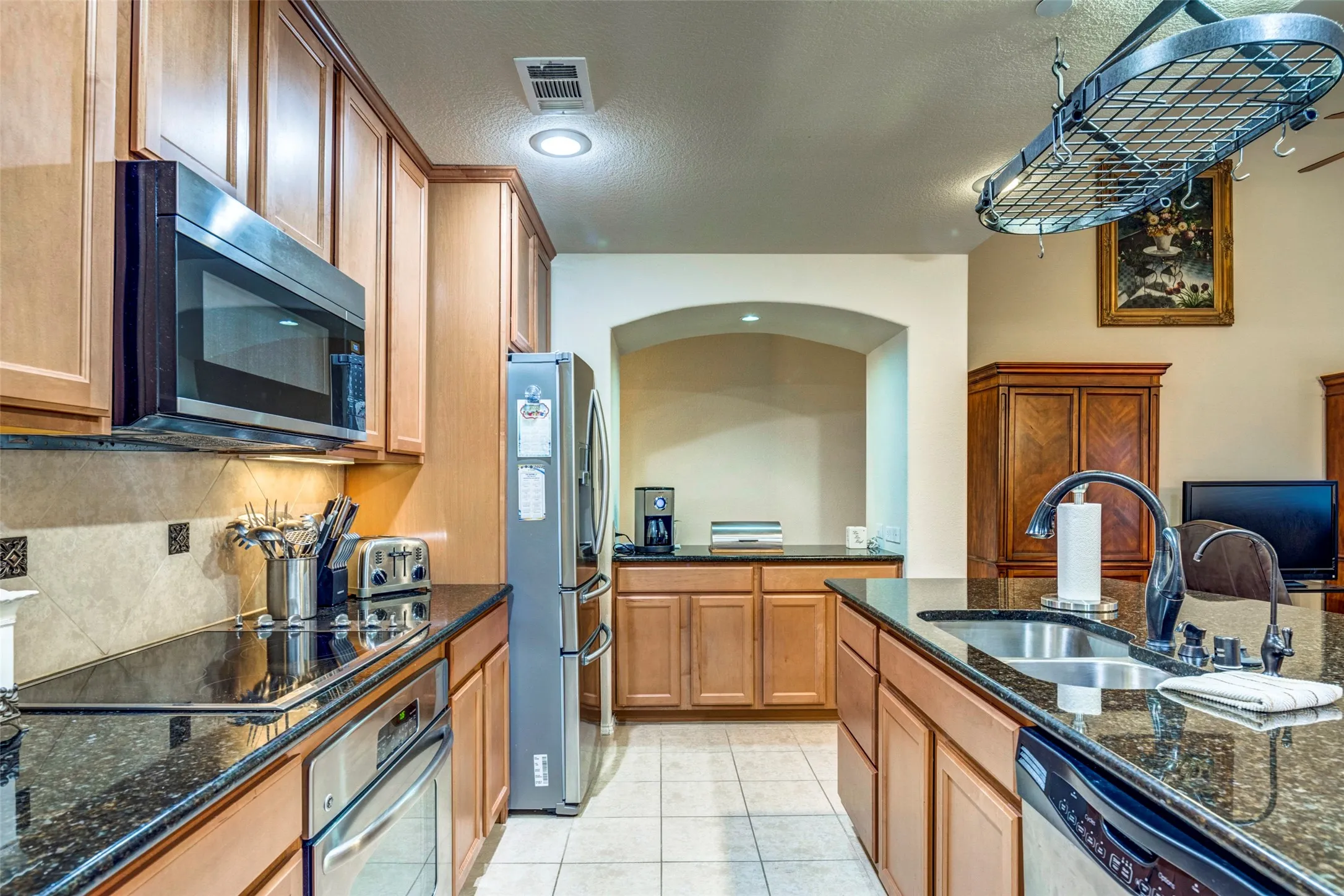 Kitchen featuring wood cabinetry, dark countertops, tile flooring, and stainless steel appliances