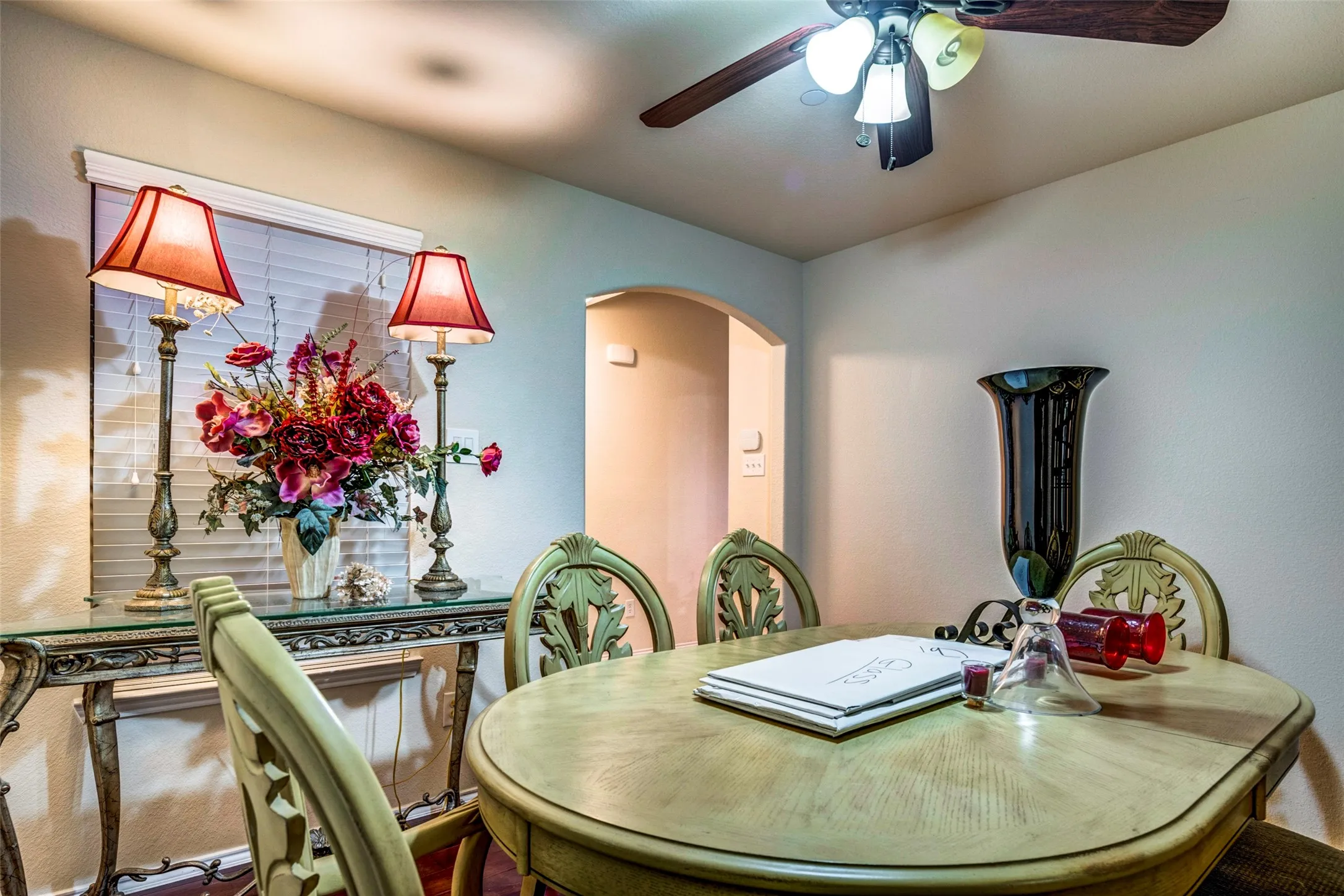 Archway entry, ceiling fan with integrated lighting, window with blinds, decorative wall sconces, accent table with glass top