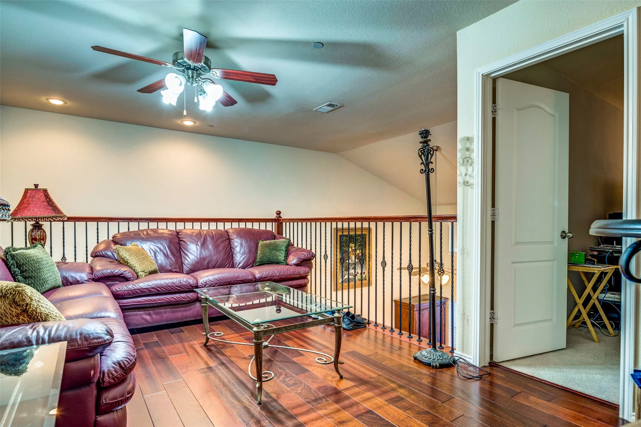 Wood-finish flooring, wrought iron and wood railing, recessed lighting, and a ceiling fan with integrated lighting