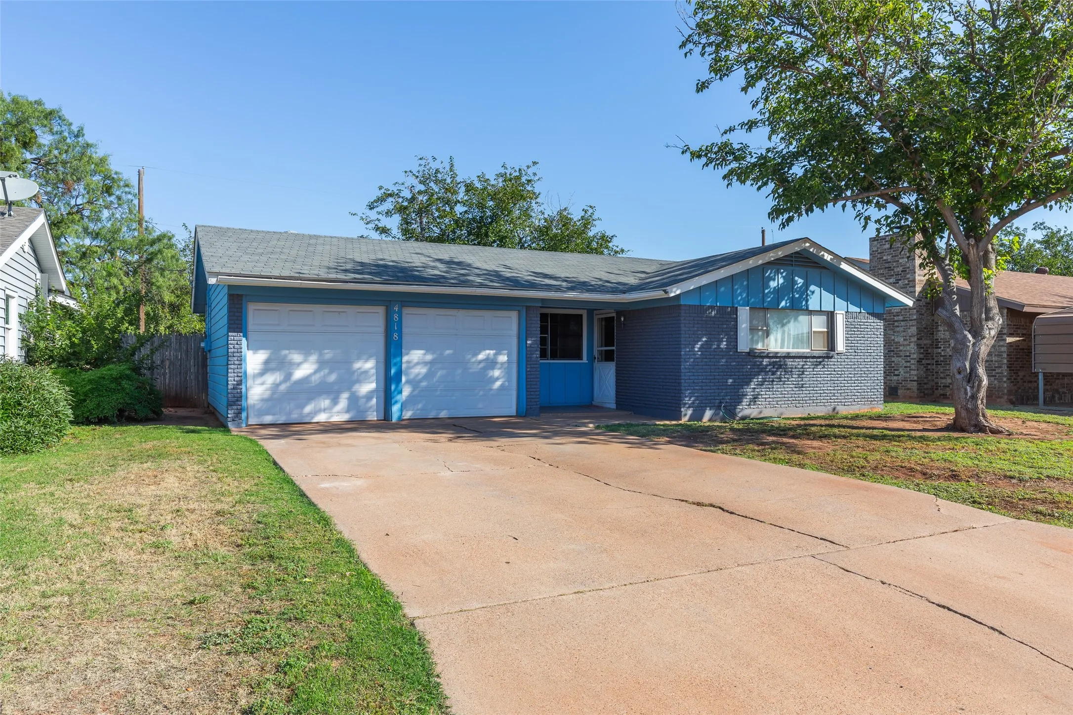 Two-car garage, brick exterior, concrete driveway, and mature trees