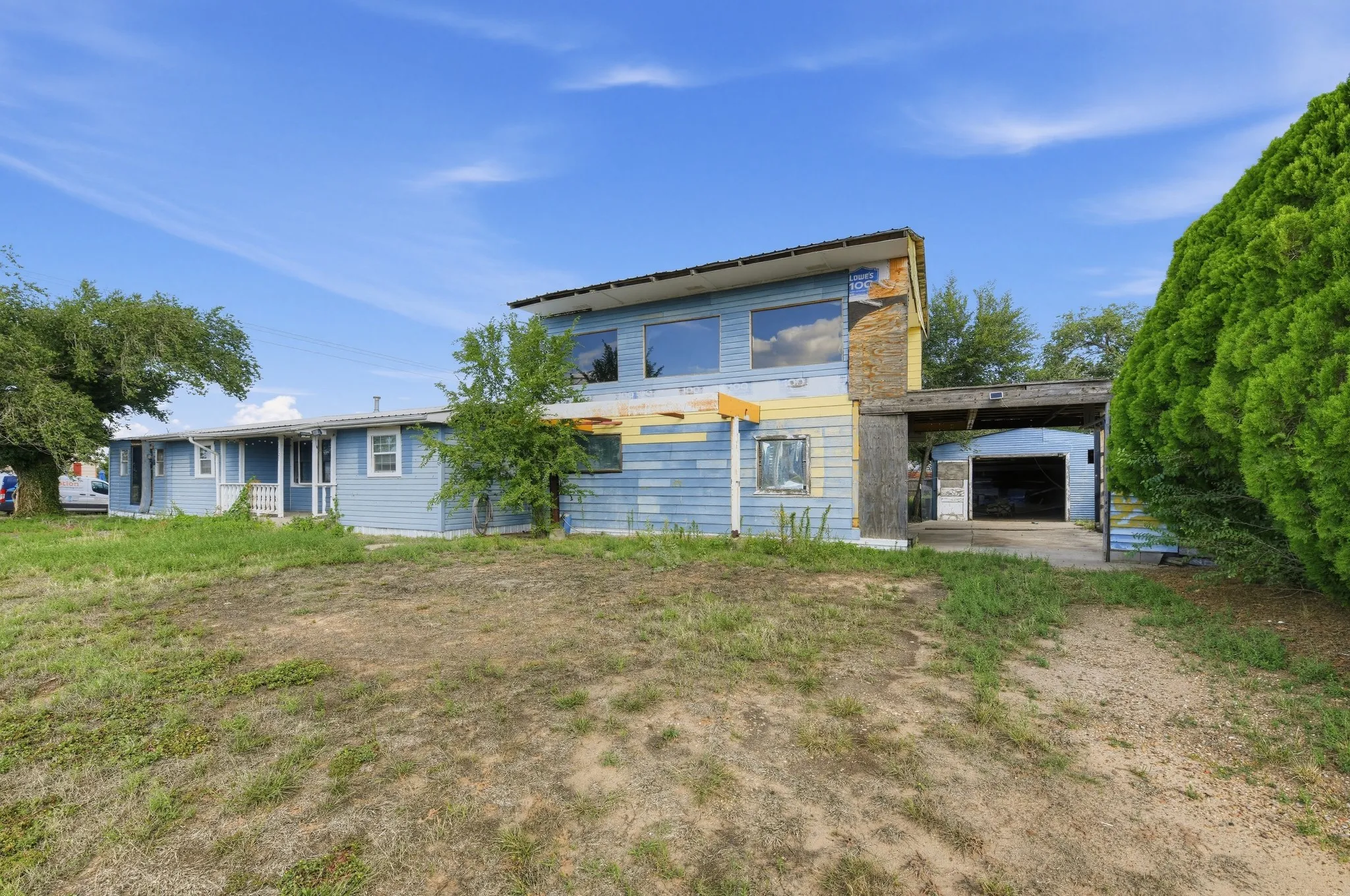 Two-story structure with blue siding, featuring multiple windows and an attached covered carport