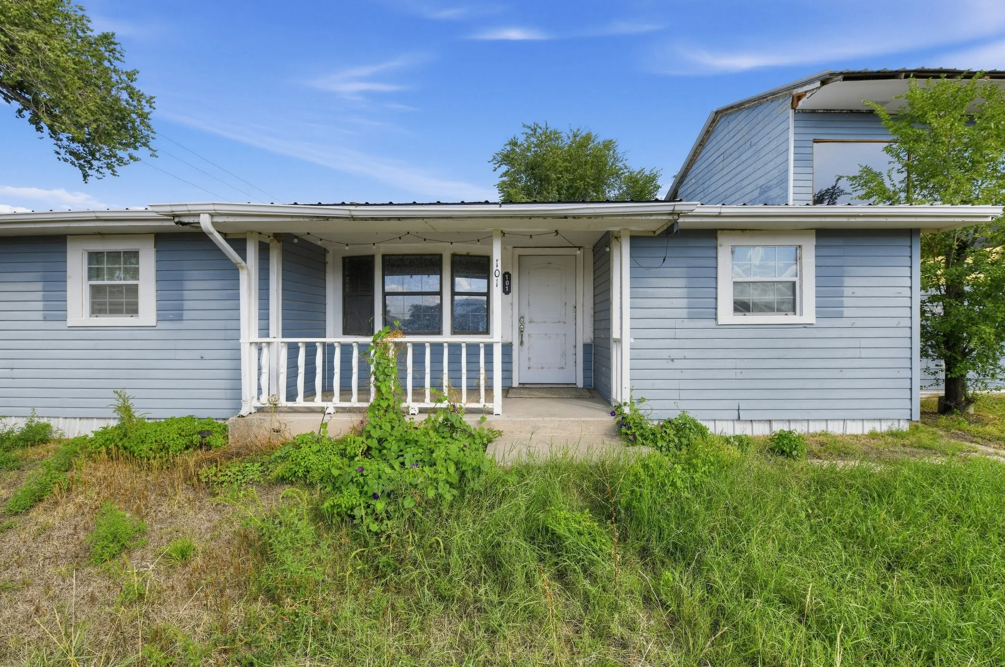 Light blue siding exterior featuring a covered porch with white railing, and multiple windows