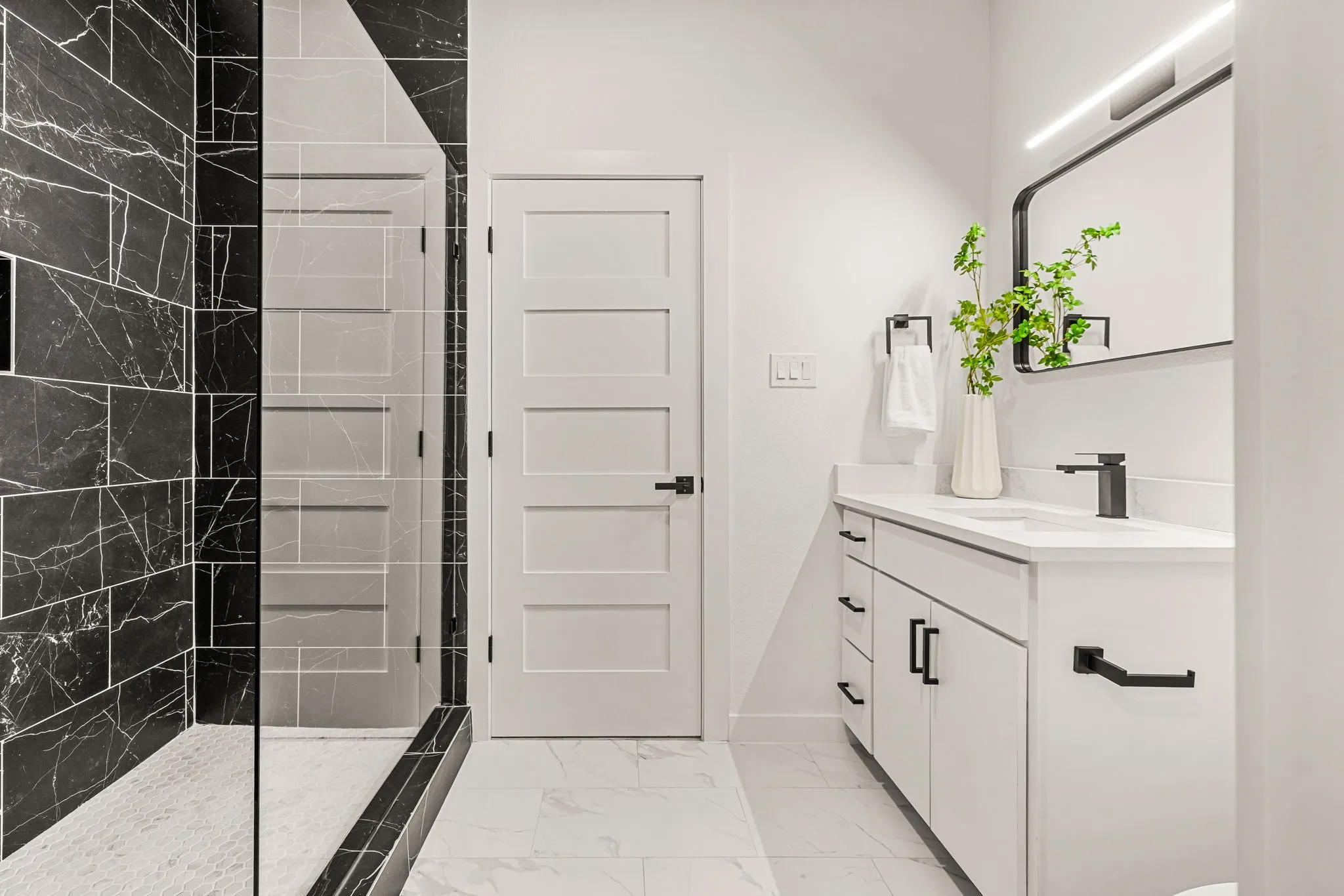 Contemporary bathroom featuring a white vanity with matte black hardware, a black-framed mirror, a walk-in shower with black marble-style tile, and white five-panel interior doors