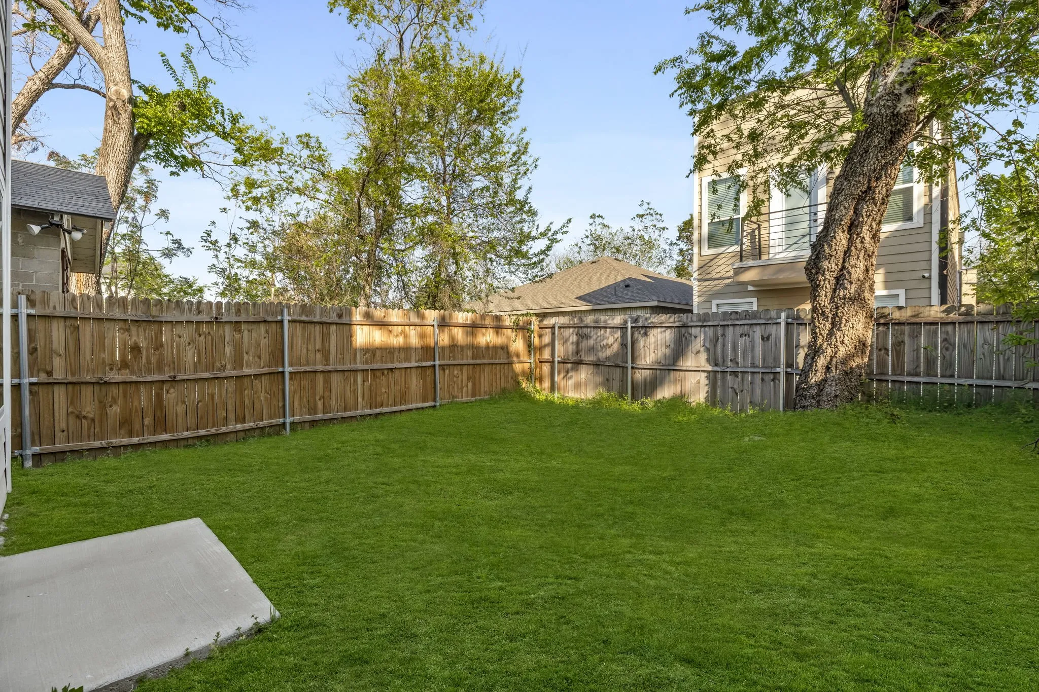 Expansive backyard featuring a manicured lawn, wood fencing, and mature trees