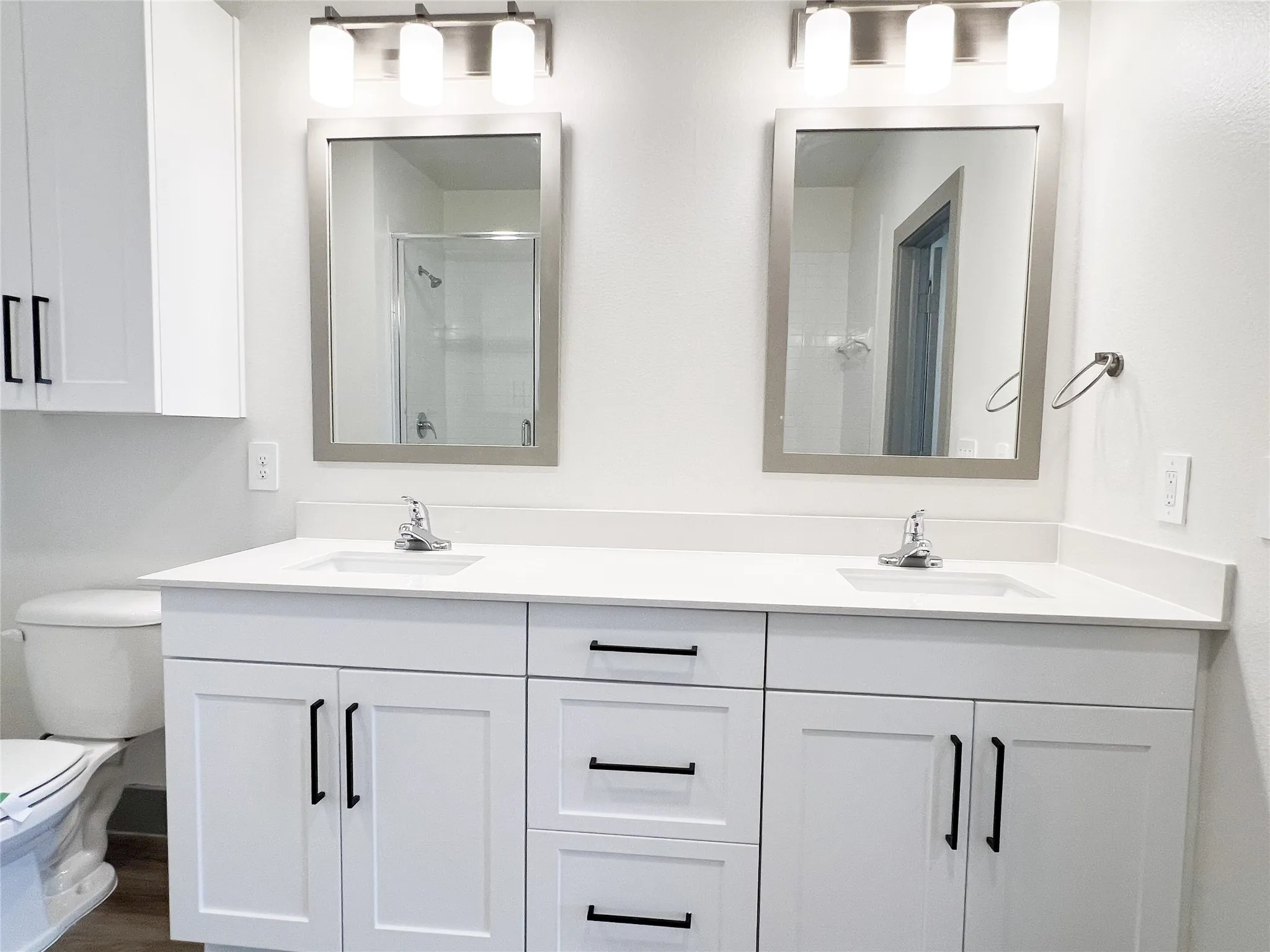 Bathroom with double vanity, a shower stall, and dark wood-style floors