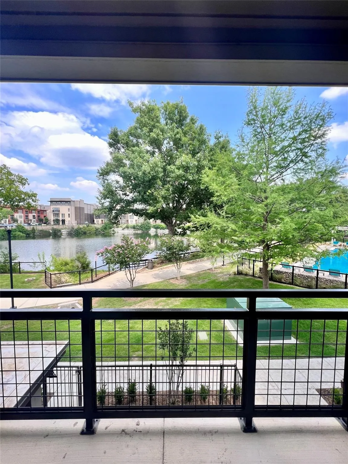 Balcony with black metal grid railing, concrete flooring, and surrounding trees