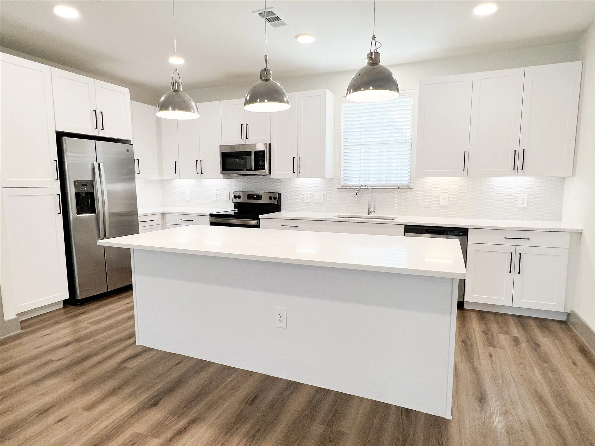 Kitchen featuring a kitchen island, hanging light fixtures, white cabinets, appliances with stainless steel finishes, and recessed lighting