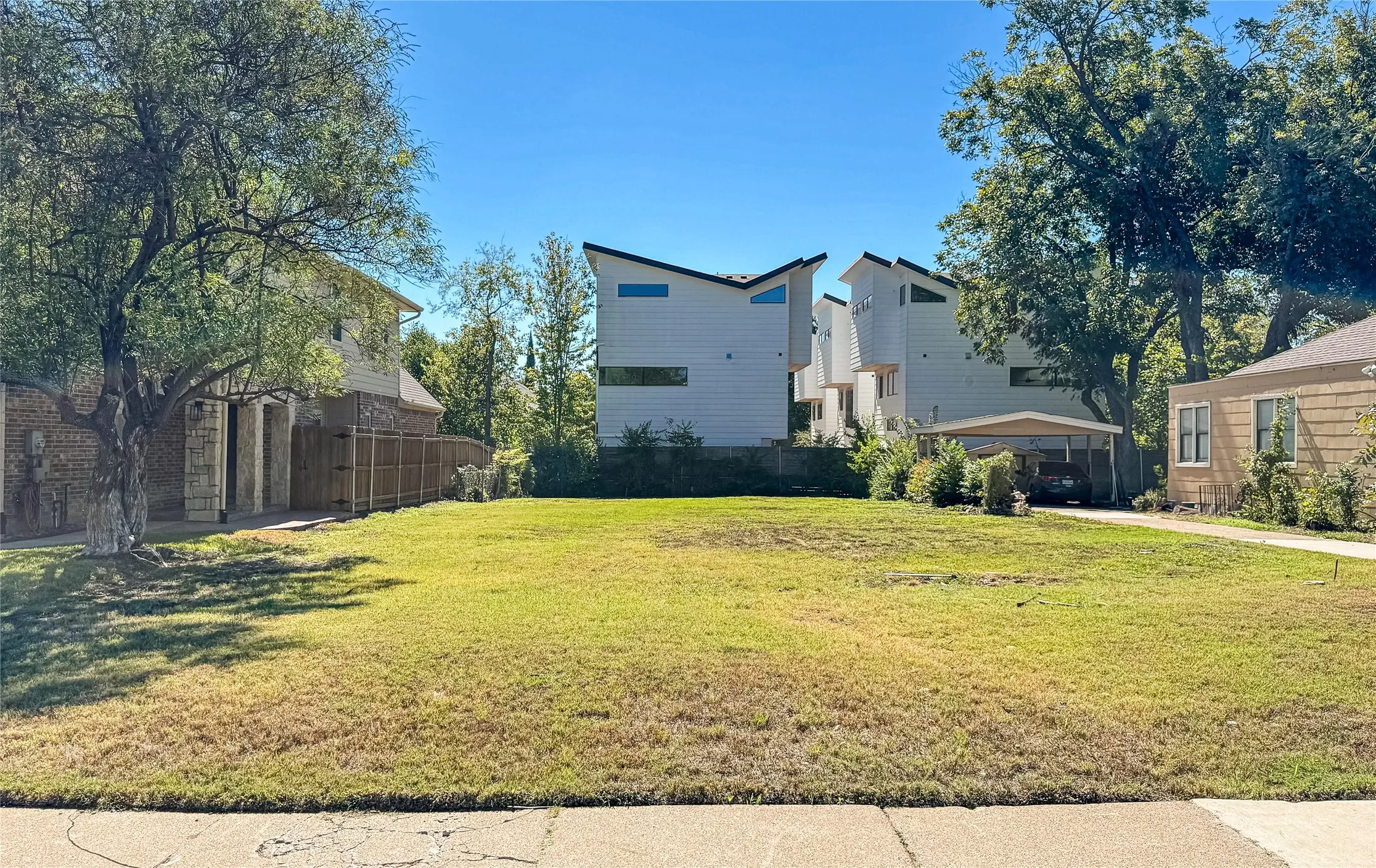 Expansive lot featuring a grass lawn, mature trees, and a concrete driveway