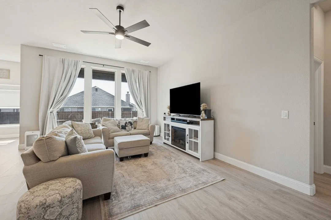 High ceilings with a ceiling fan, large window for natural light, wood-finish flooring, and light-colored walls