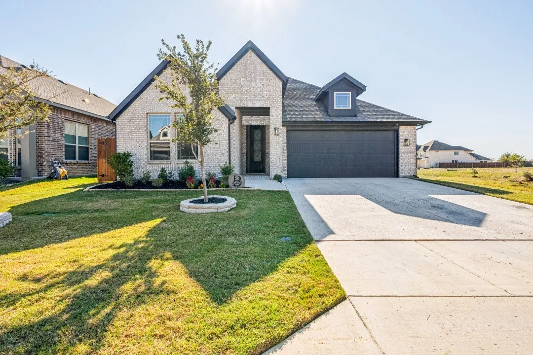 Brick exterior with dark gray roof, two-car garage, concrete driveway, and front lawn landscaping