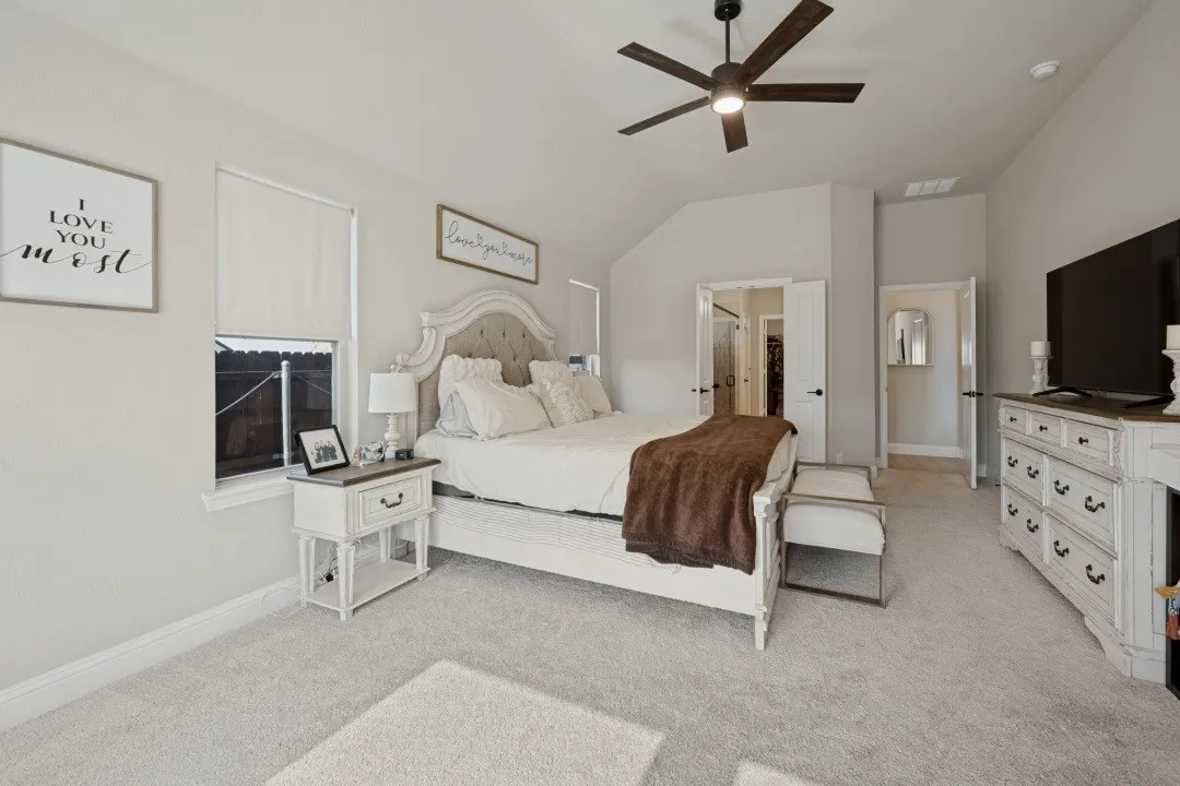 Vaulted ceiling with a ceiling fan, light-colored walls, and light-colored carpet flooring