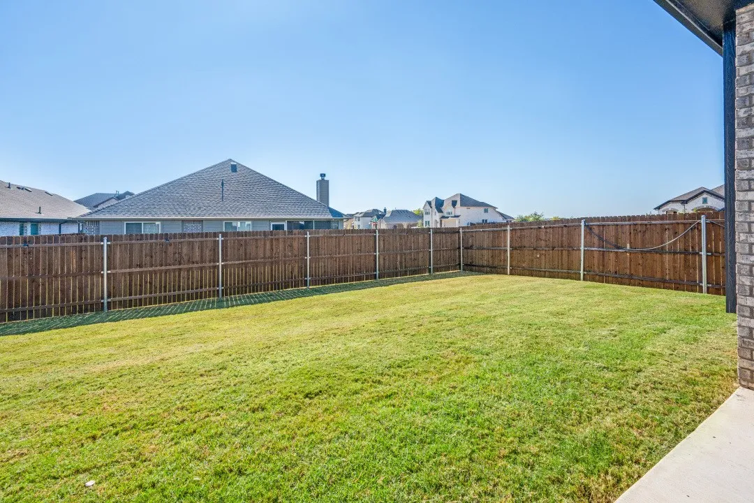 Expansive backyard featuring a manicured lawn, wood privacy fence, and concrete patio