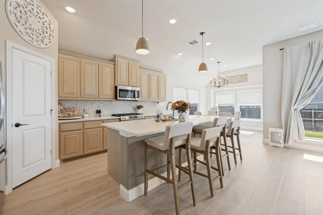 Well-appointed kitchen featuring light-toned cabinetry, stainless steel appliances, a white tile backsplash, and an expansive island